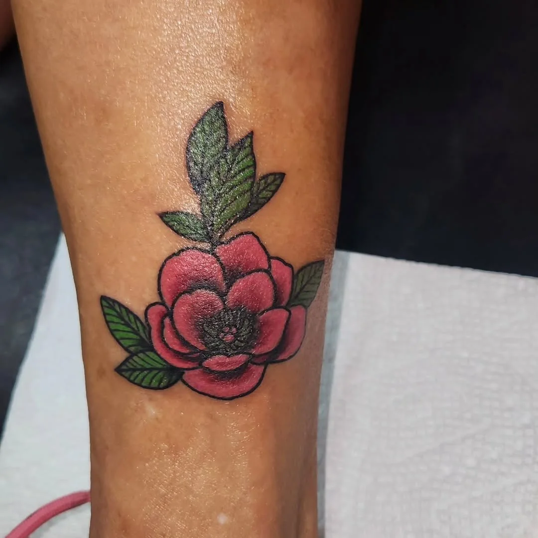 Colorful tattoo of a red flower with green leaves on a person's arm.