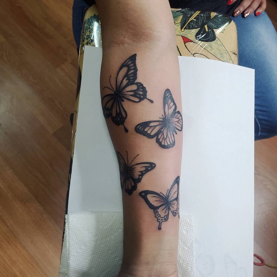 A person's forearm with four black outlined butterfly tattoos.