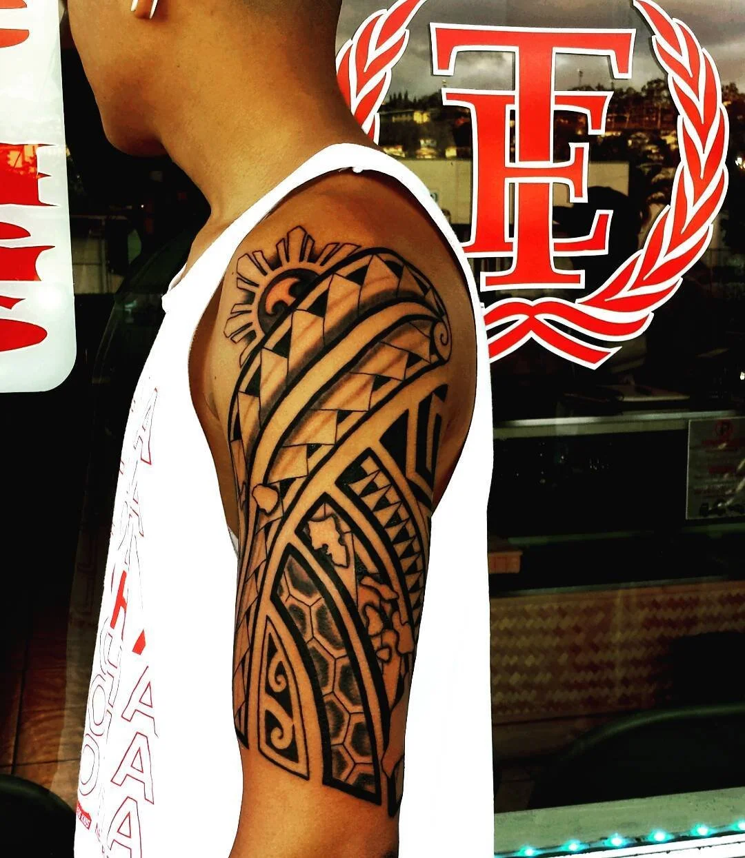 Black Polynesian-style tattoo on person's upper arm featuring geometric patterns and natural elements.