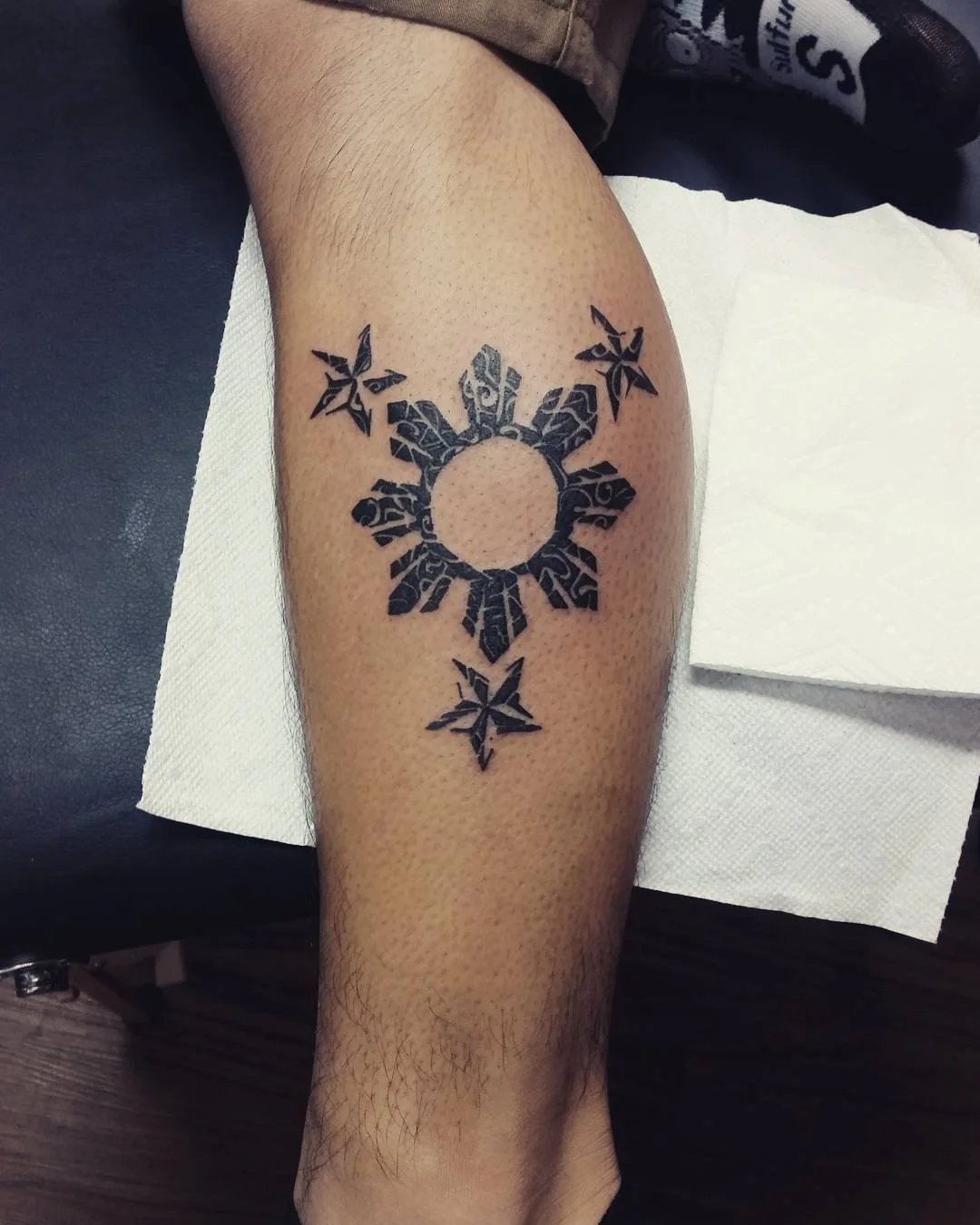 Tattoo of the Hylian Crest from The Legend of Zelda on a person's calf, featuring a stylized bird and a ring, with three star shapes above and below.