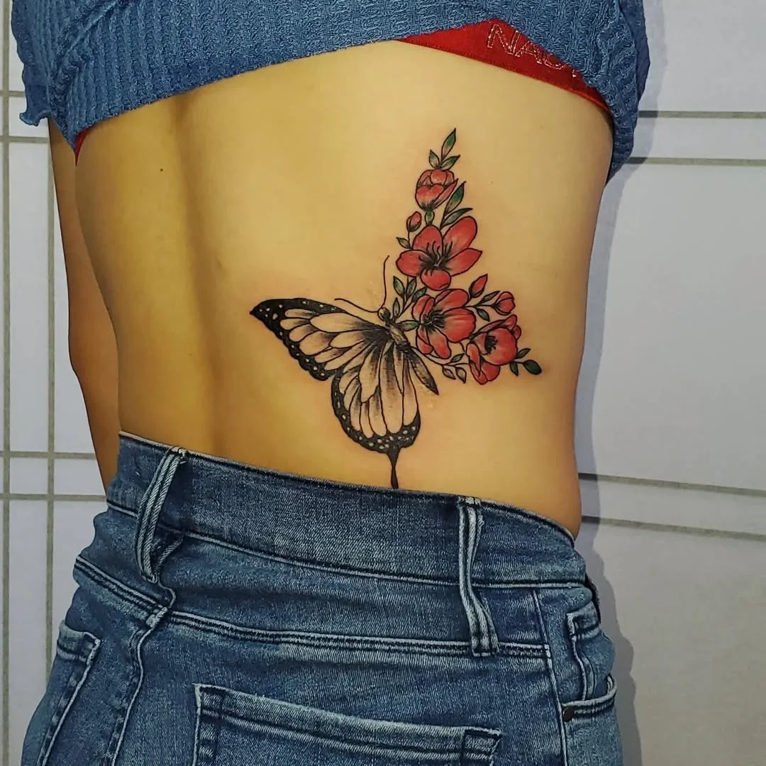 Tattoo of a butterfly with vibrant orange flowers on the person's side, partially visible in blue denim shorts.