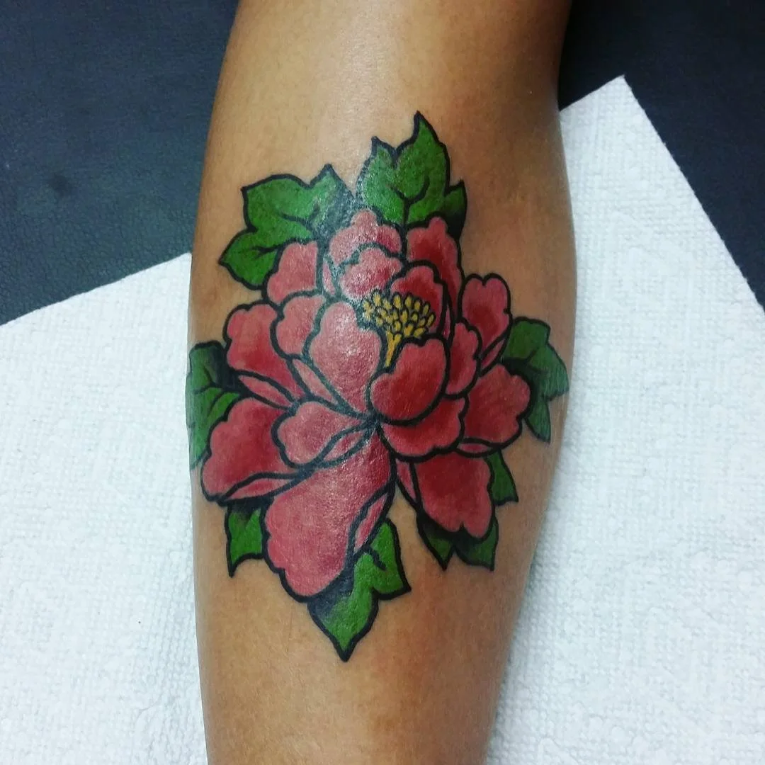 Colorful tattoo of a red flower with green leaves on a person's arm.
