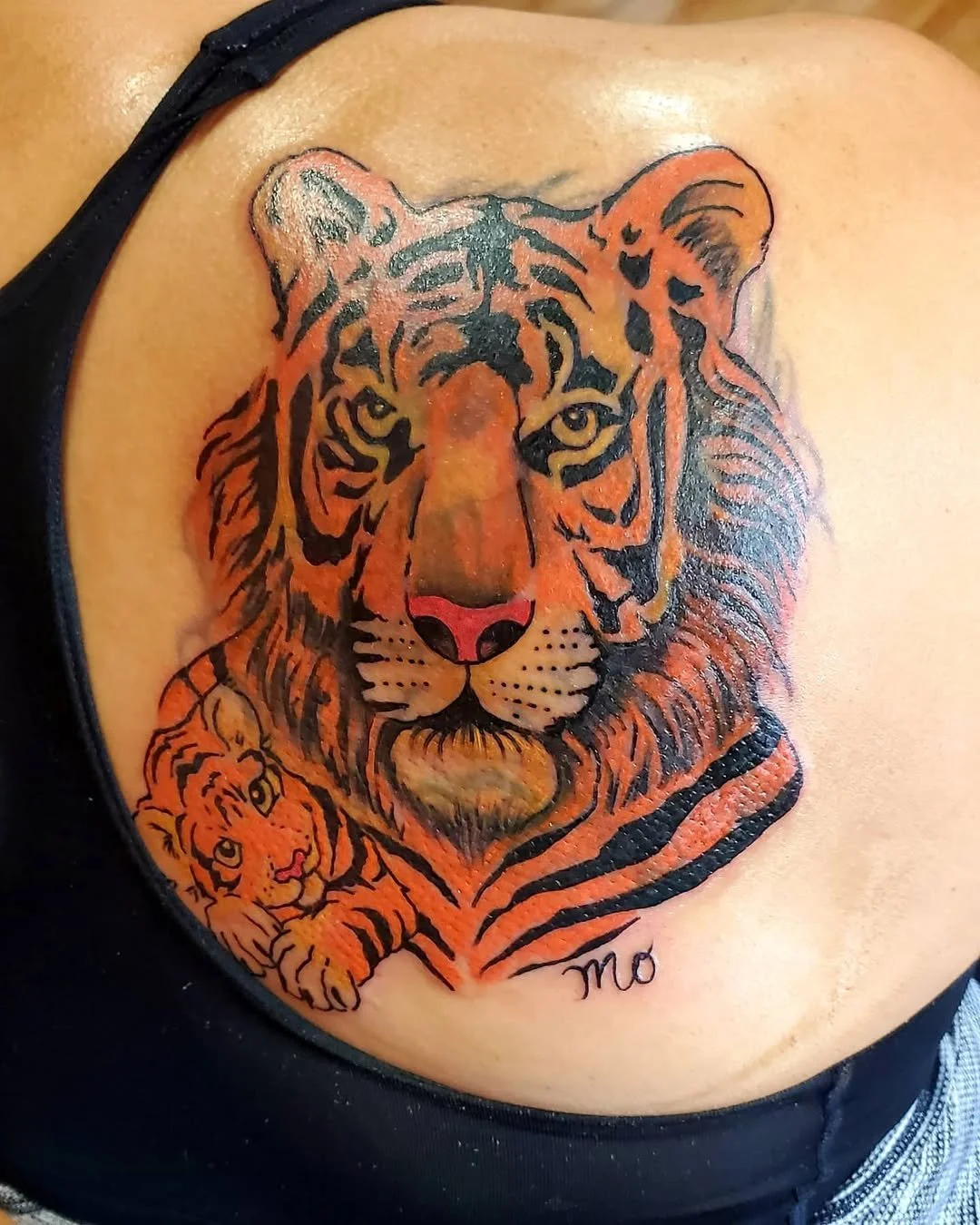 Tattoo of a tiger's face with a smaller tiger beneath, both in black and orange ink, on a person's chest.