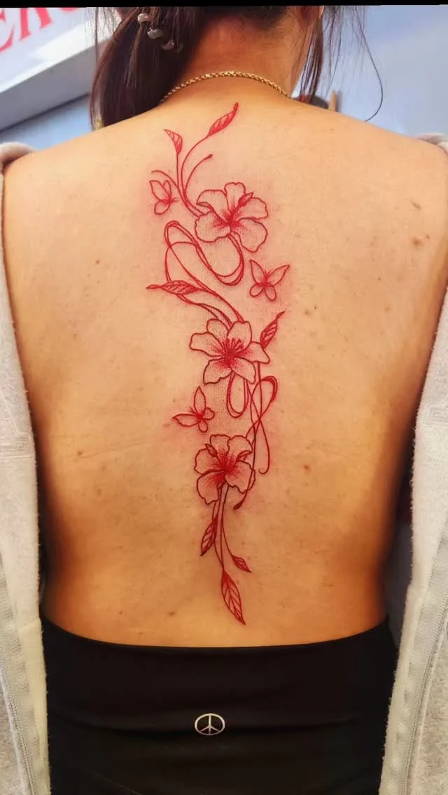 Red floral tattoo with butterflies on person's back.