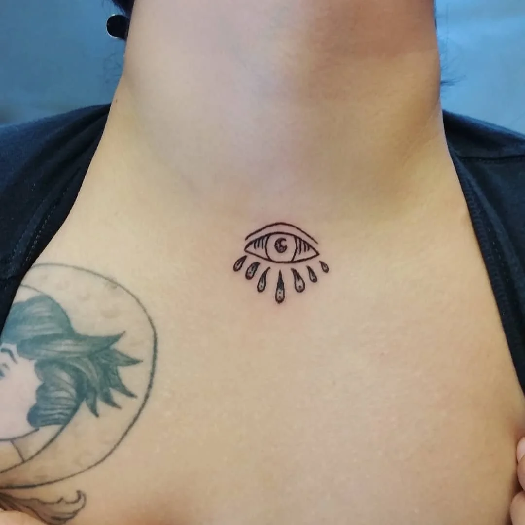Tattoo of an eye with tears falling beneath it on a person's chest.