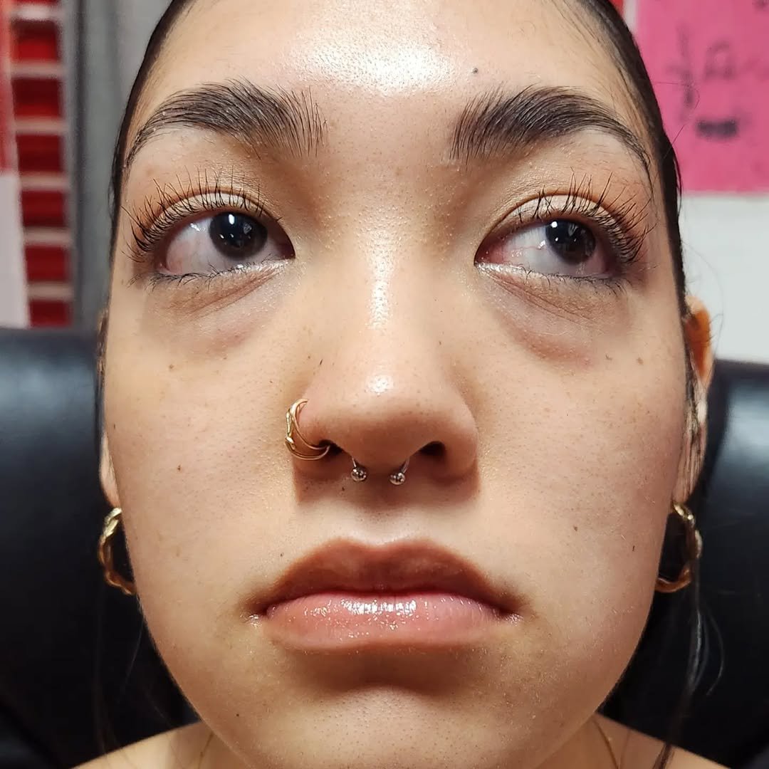 Close-up of a young woman's face with hoop earrings and septum piercing, looking upward with relaxed expression.