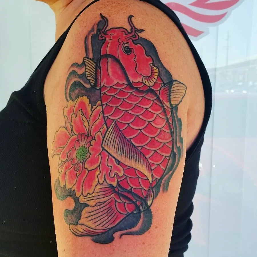 Tattoo of a koi fish and a flower on a person's upper arm.