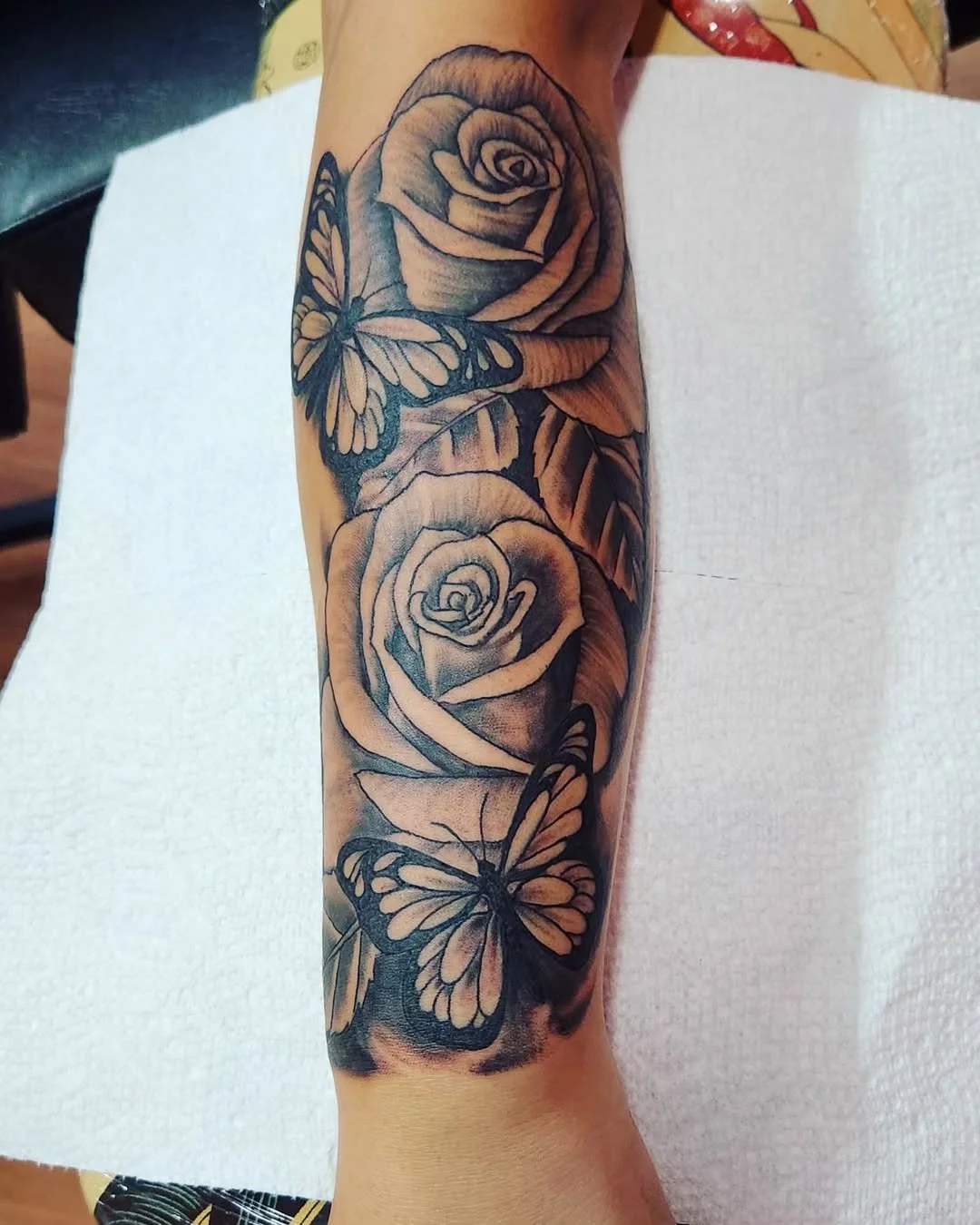 Tattoo of two roses and two butterflies on a person's forearm.
