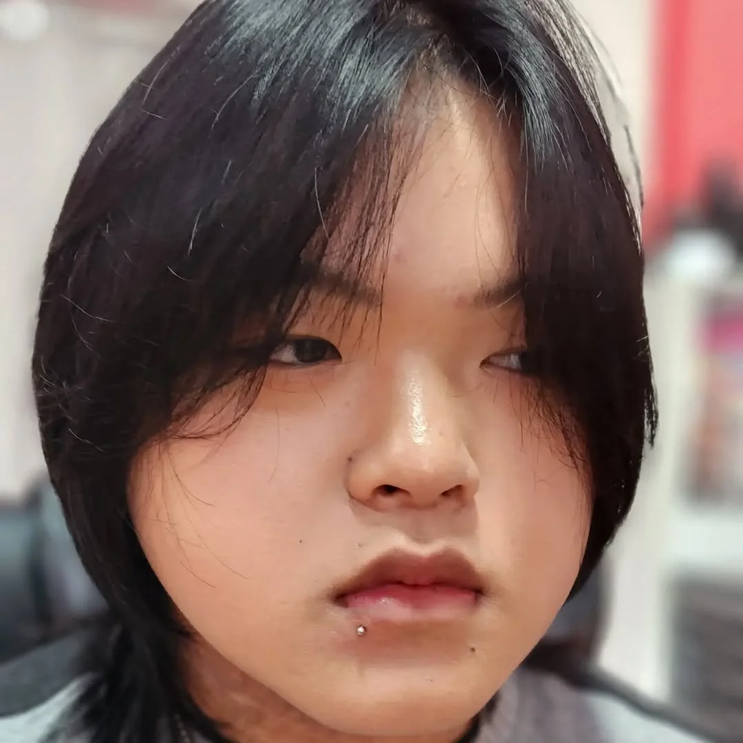 Close-up of a person with medium-length dark hair, a lip piercing, and a neutral expression.