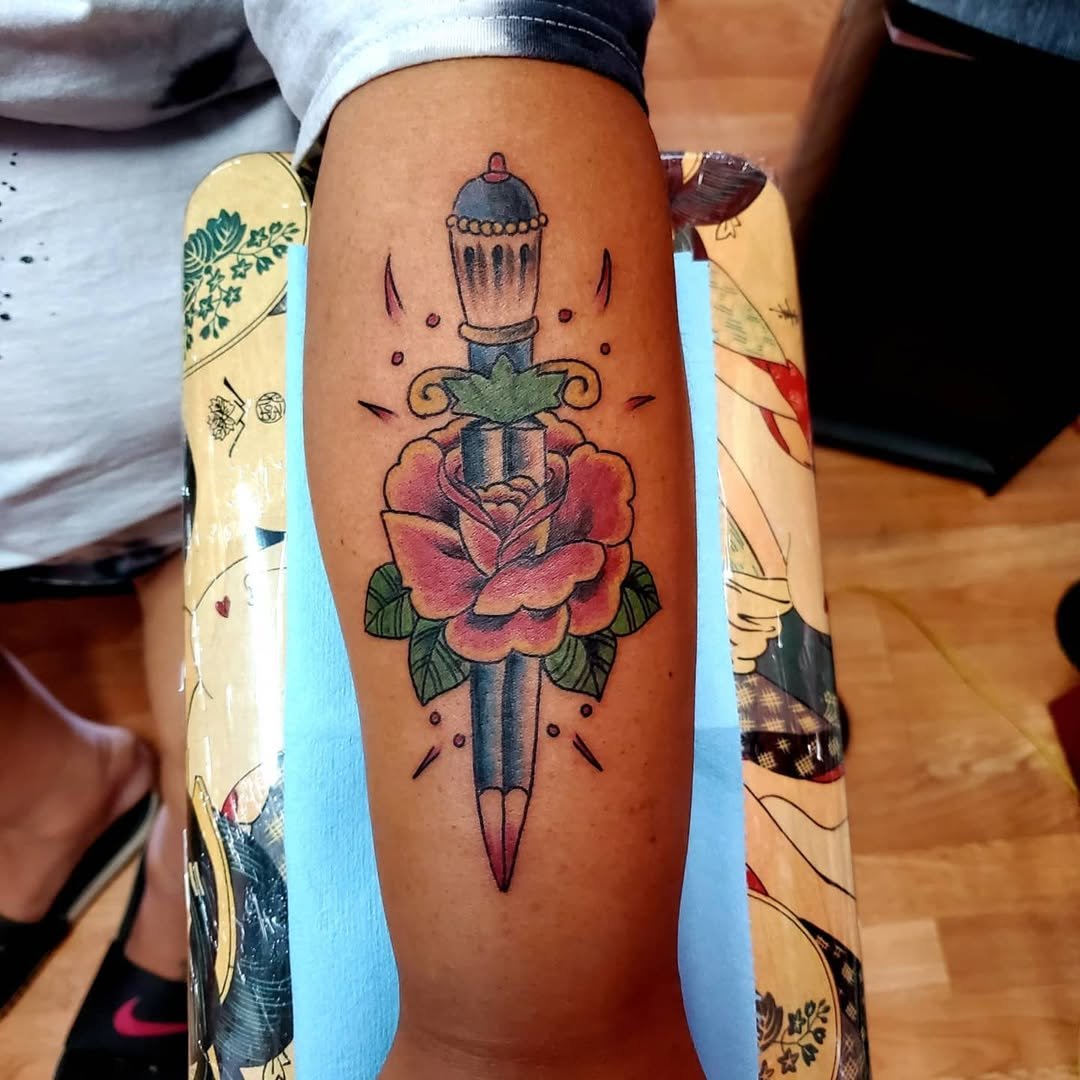Colorful tattoo of a dagger with a flower and a cupcake on the arm.