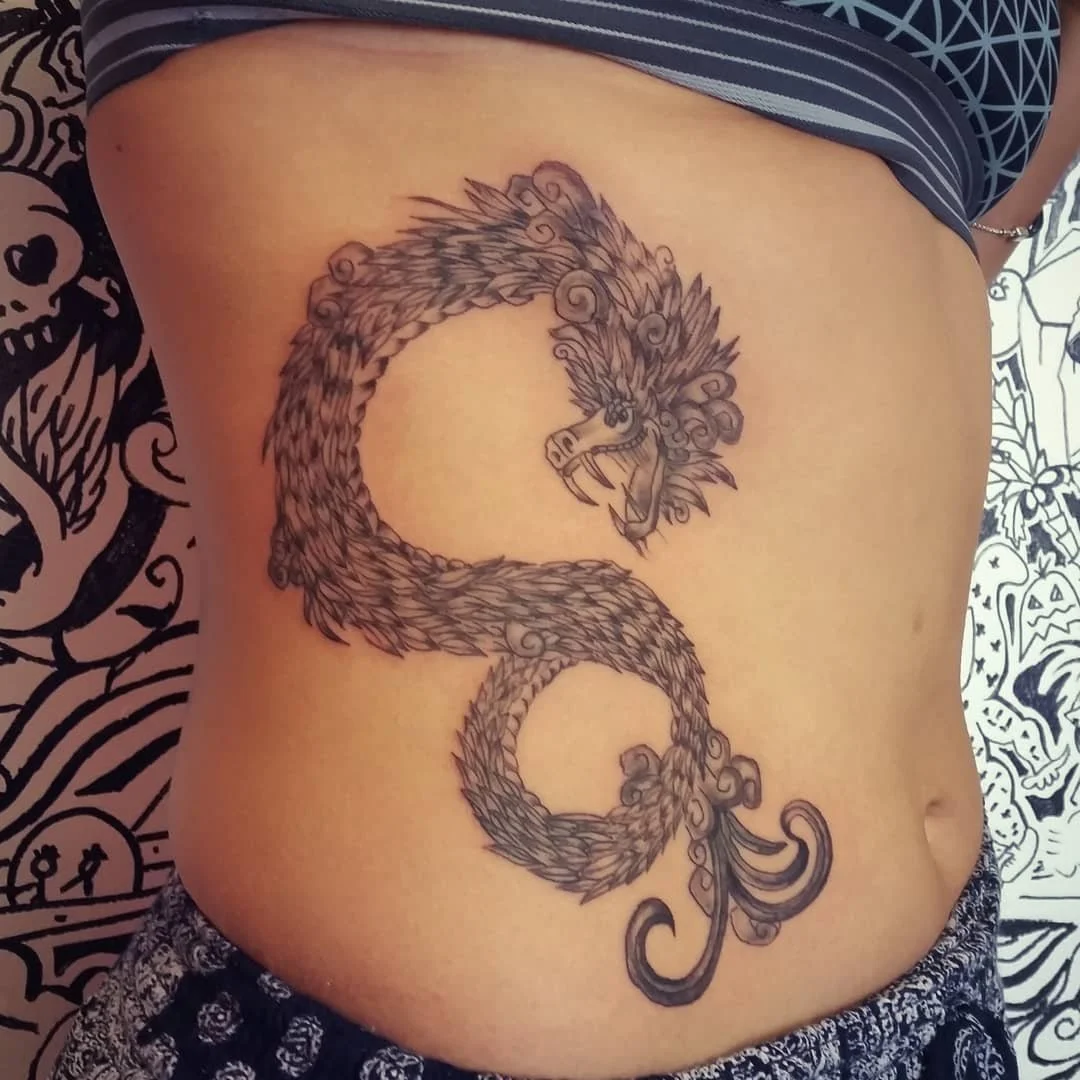 Tattoo of a stylized dragon on a person's side, featuring a detailed, fierce face and a long, winding tail.