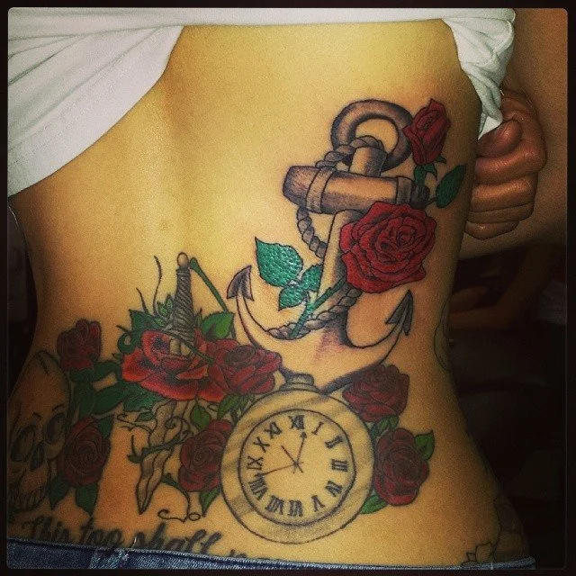 Colorful tattoo on side of person's torso featuring an anchor with roses and a clock with Roman numerals.
