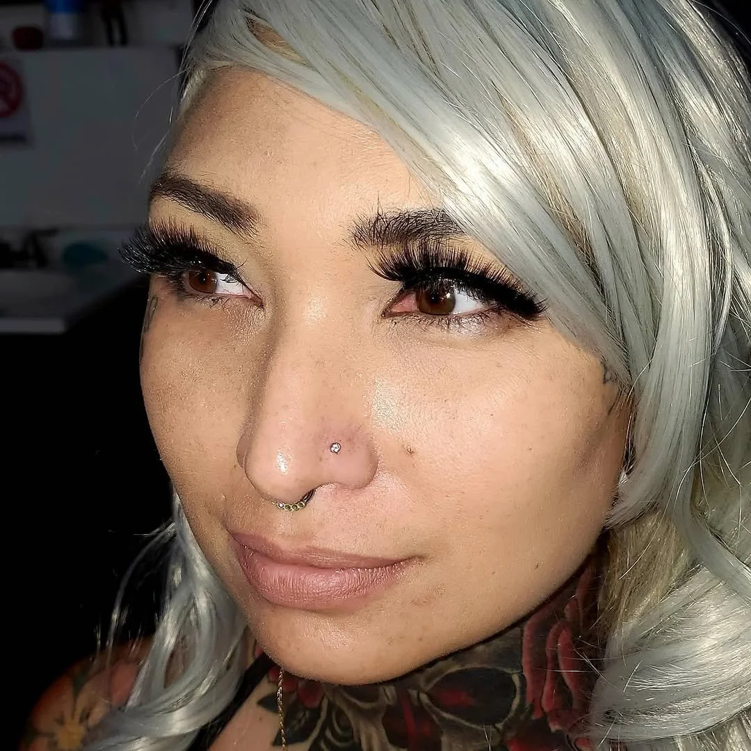 Close-up of a woman with silver hair, brown eyes, and prominent makeup, including long eyelashes.