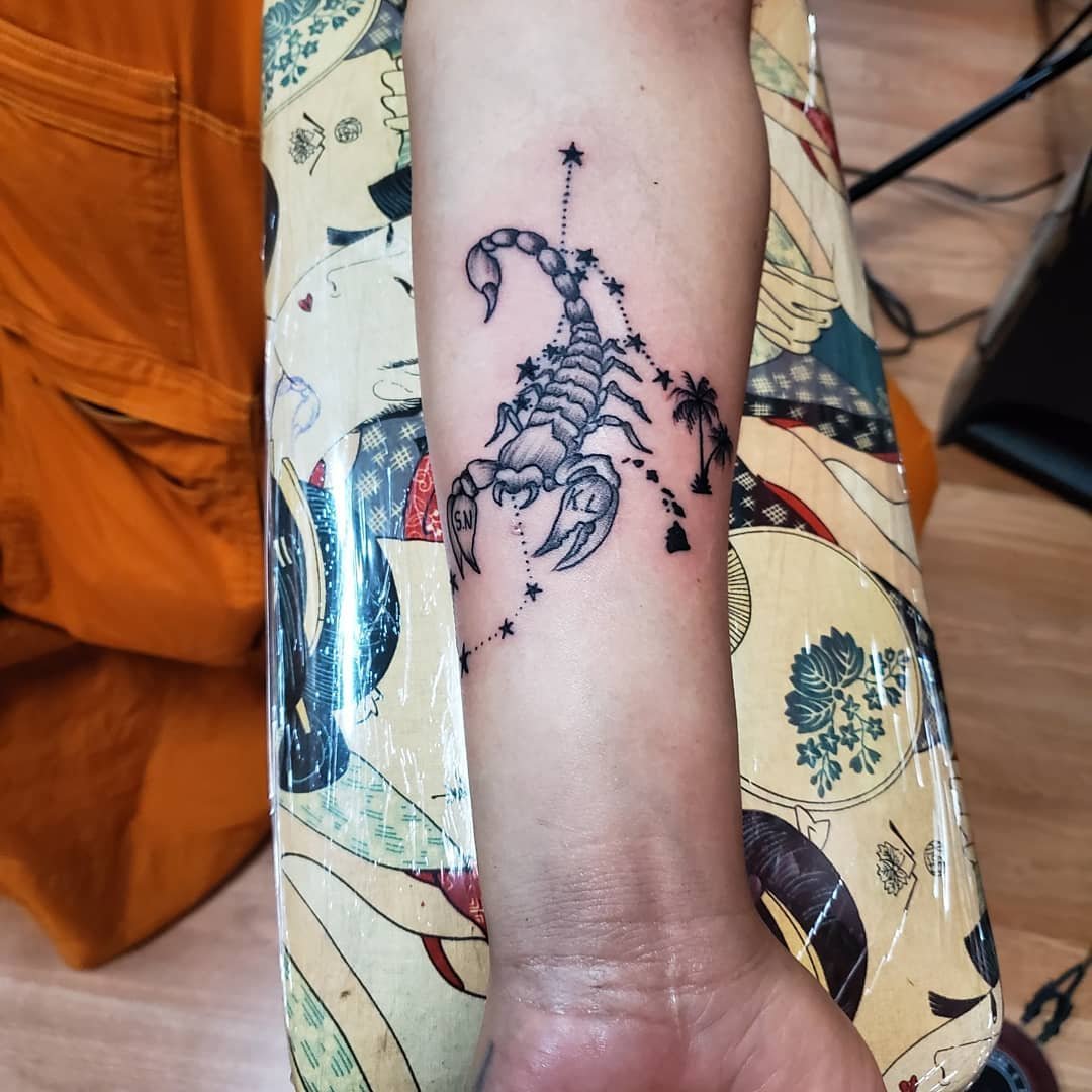 Tattoo of a realistic scorpion with celestial elements like stars and a palm tree, with ink and art style typical of line work tattoos.