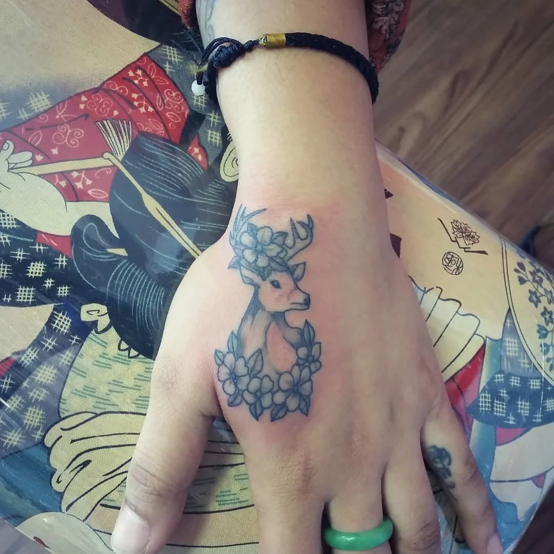 Tattoo of a deer head with antlers surrounded by flowers on a person's hand.