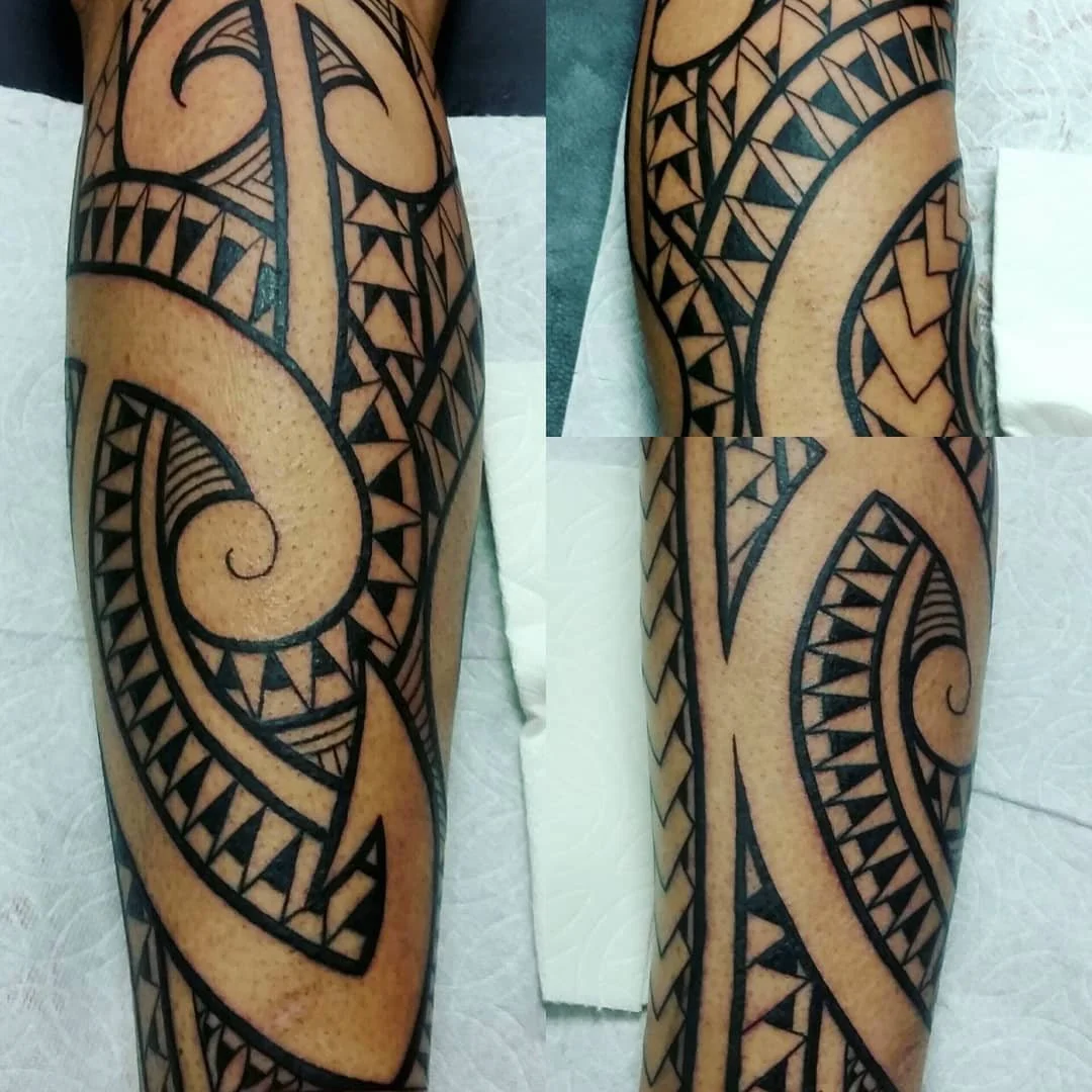 A Polynesian-style tribal tattoo running along the upper arm, featuring bold black geometric patterns, spirals, triangles, and lines.