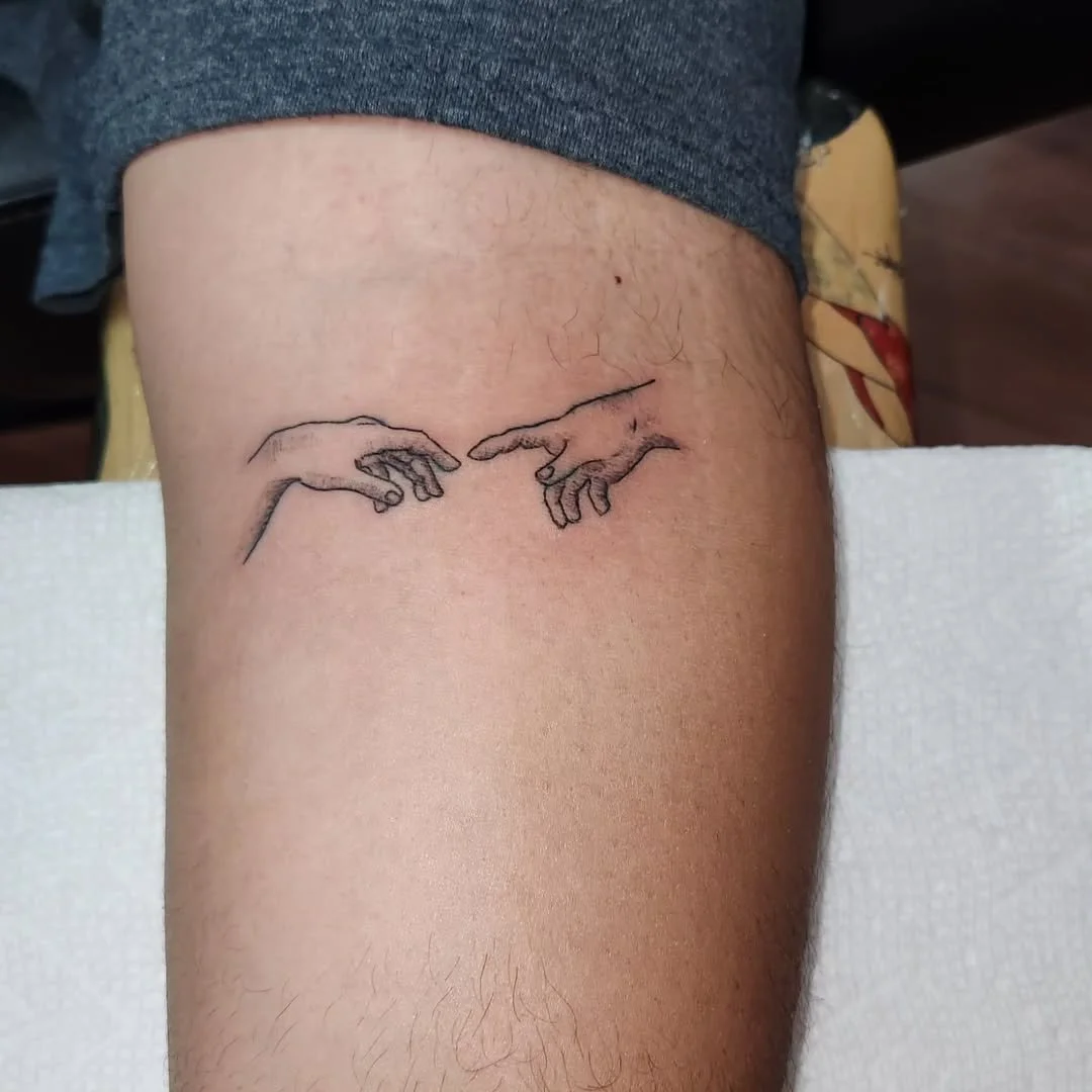 Tattoo of two hands reaching toward each other on a person's upper leg.