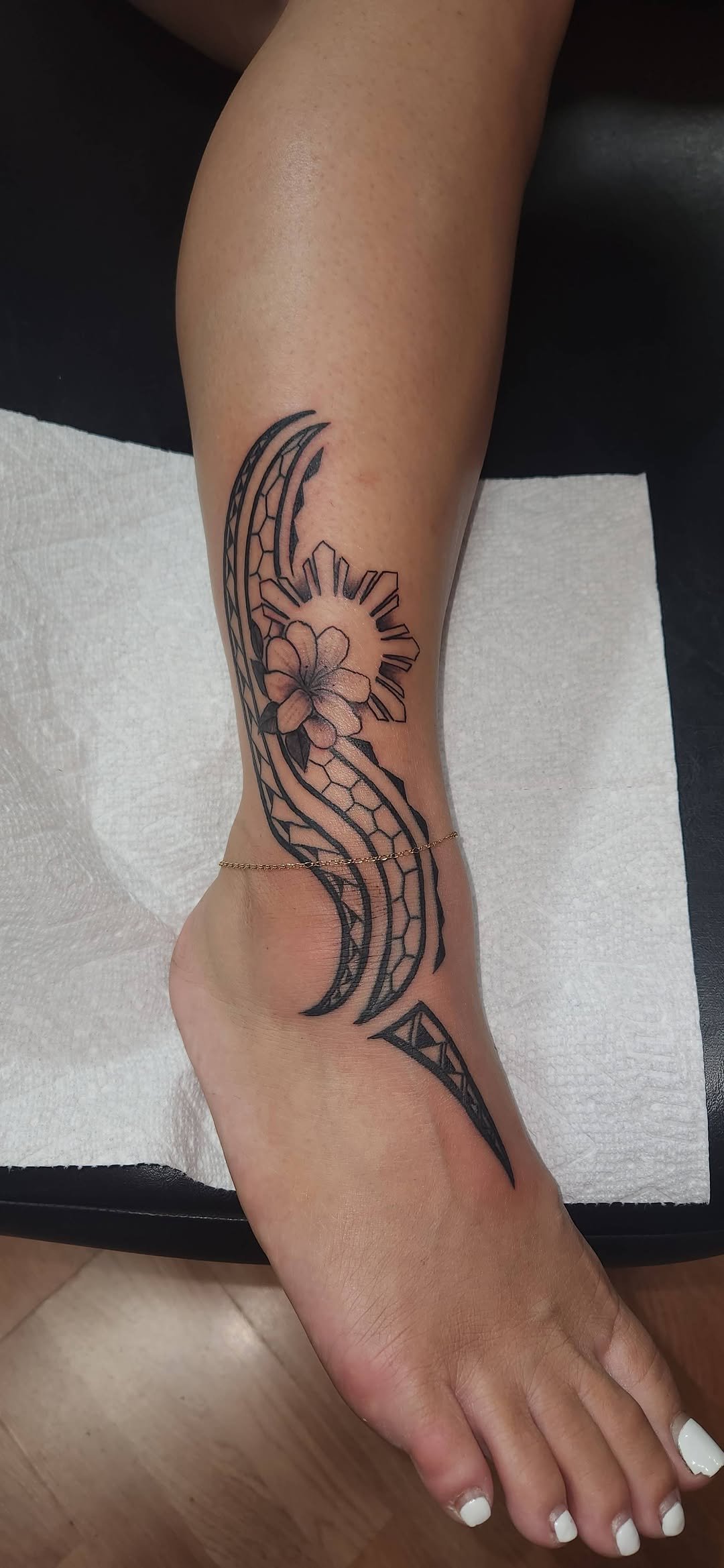 Black and gray tattoo of a flower and tribal patterns on a person's calf and foot.