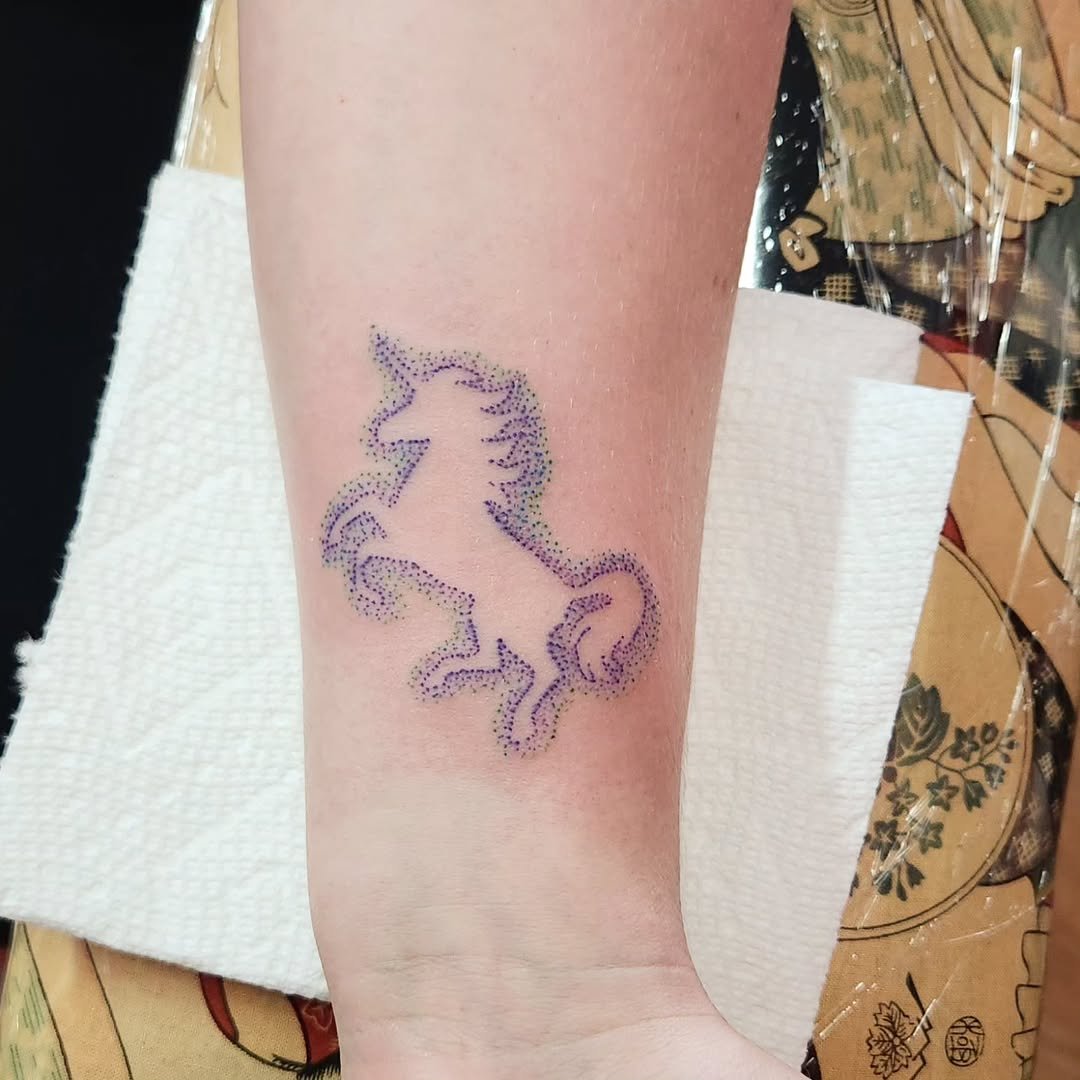Tattoo of a purple, dotted unicorn on person's forearm.