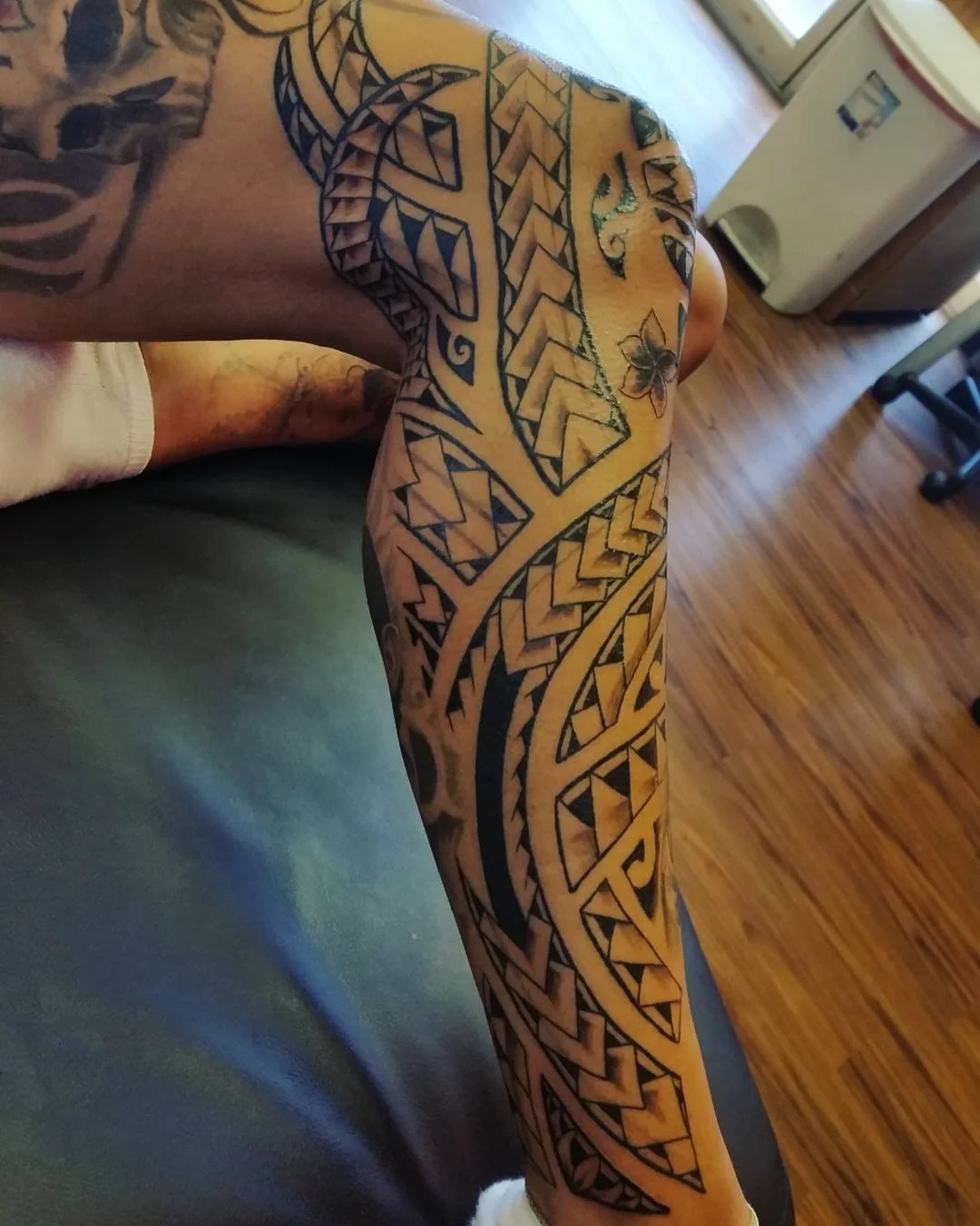 A person with a full sleeve tattoo of intricate black tribal and geometric designs covering their arm and part of their shoulder.