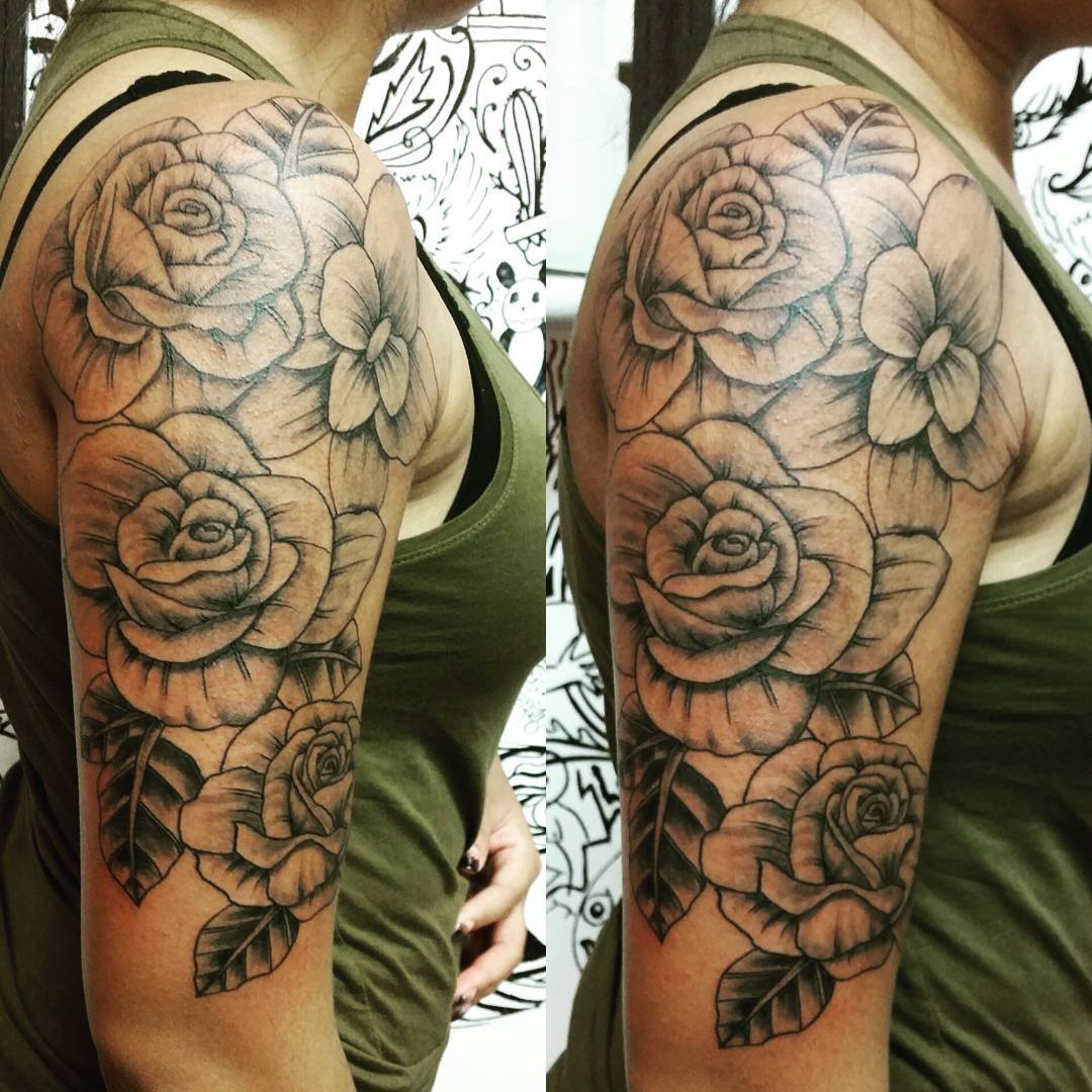 Black and gray tattoo of roses and leaves on a person's upper arm and shoulder.