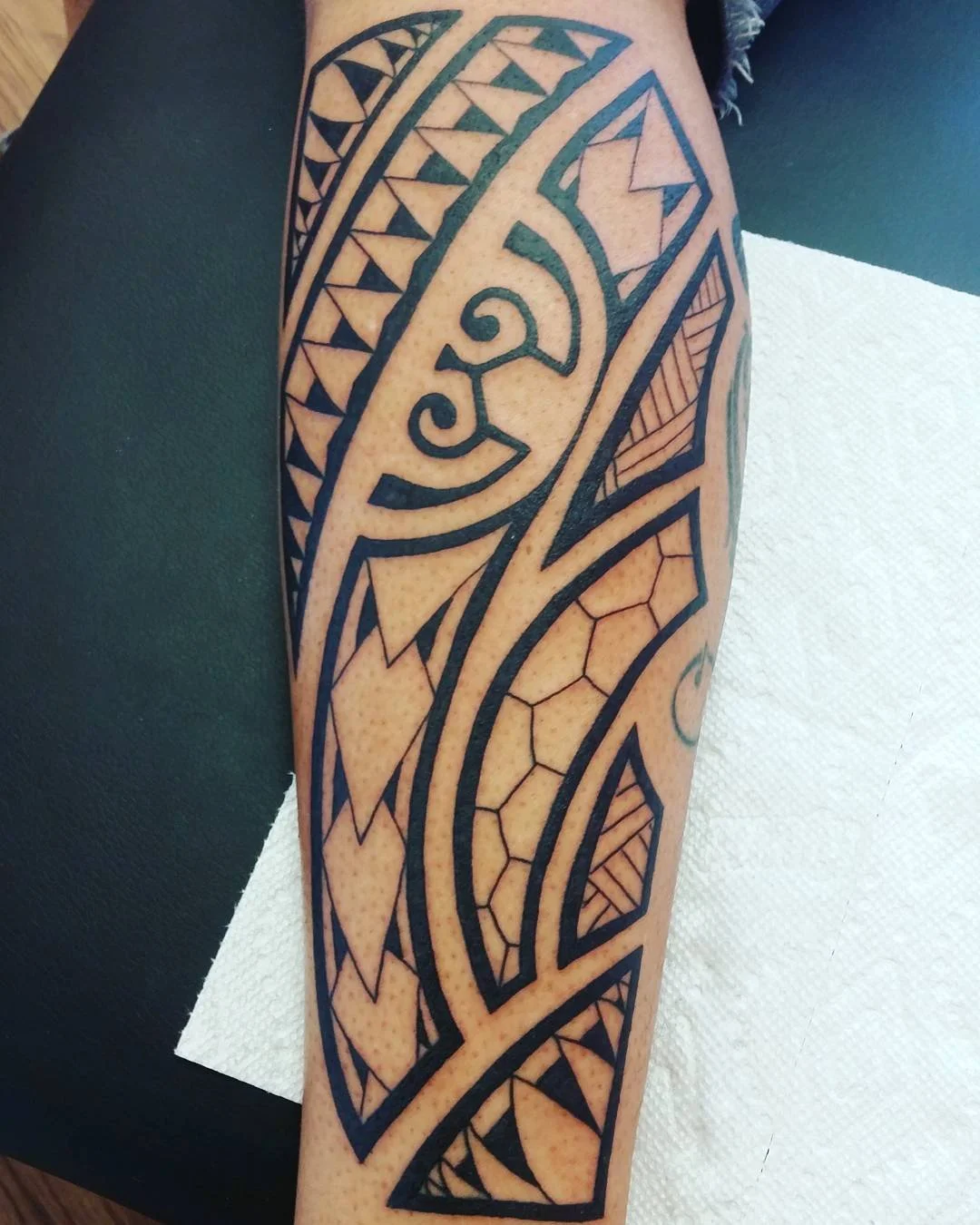 A Polynesian-style tribal tattoo on person's arm featuring bold black geometric patterns and intricate line work.