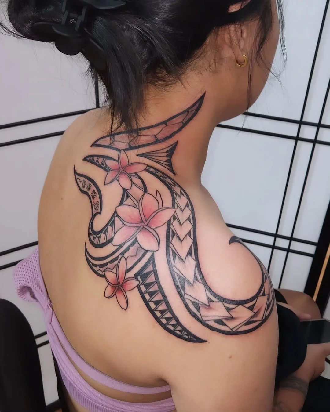 A woman's shoulder and back tattoo featuring flowers, tribal patterns, and geometric designs in black and pink ink.