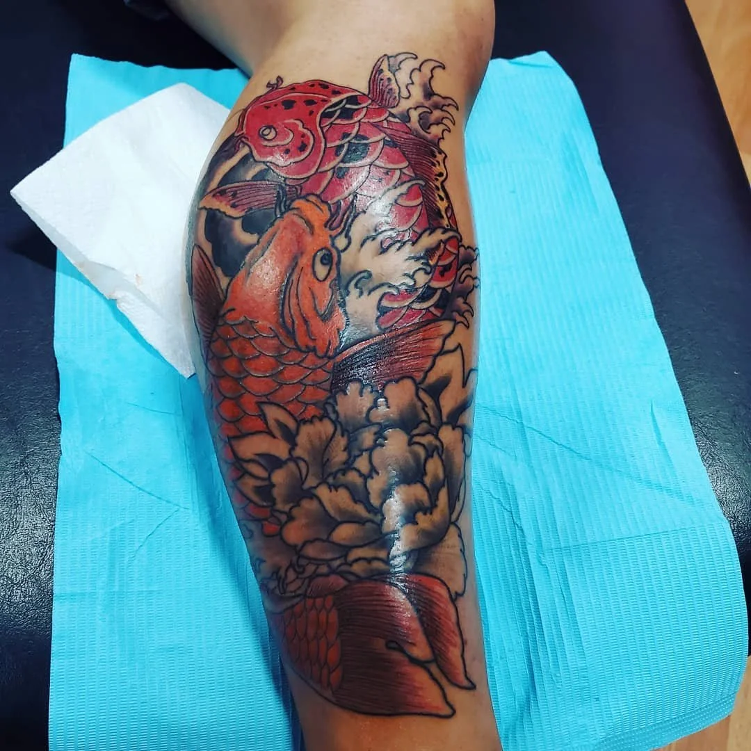 Colorful tattoo of a koi fish, a bird, and flowers on a person's arm.