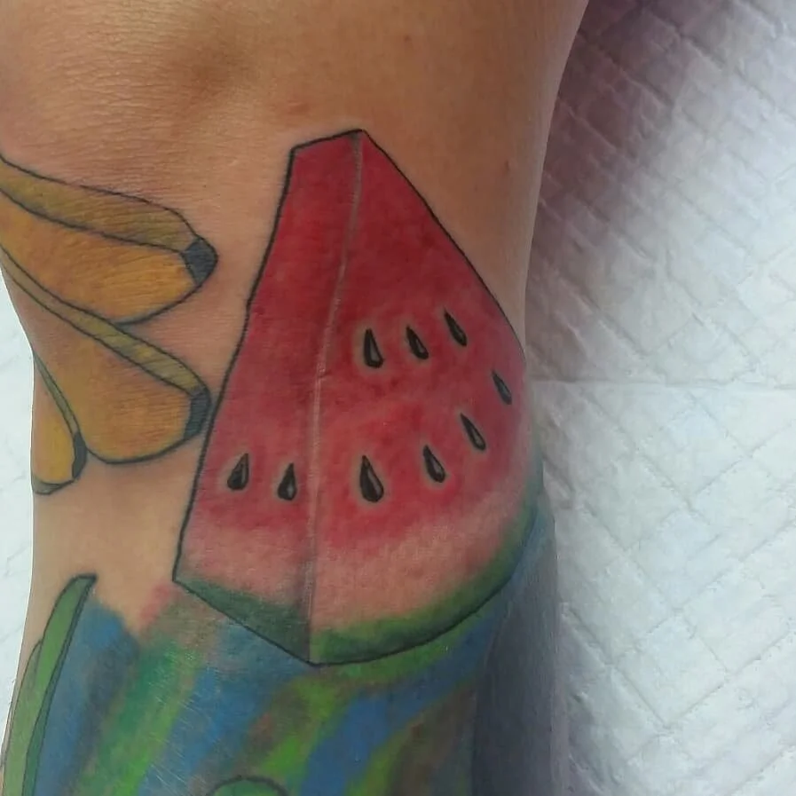 Colorful tattoo of a watermelon slice on a person's skin.