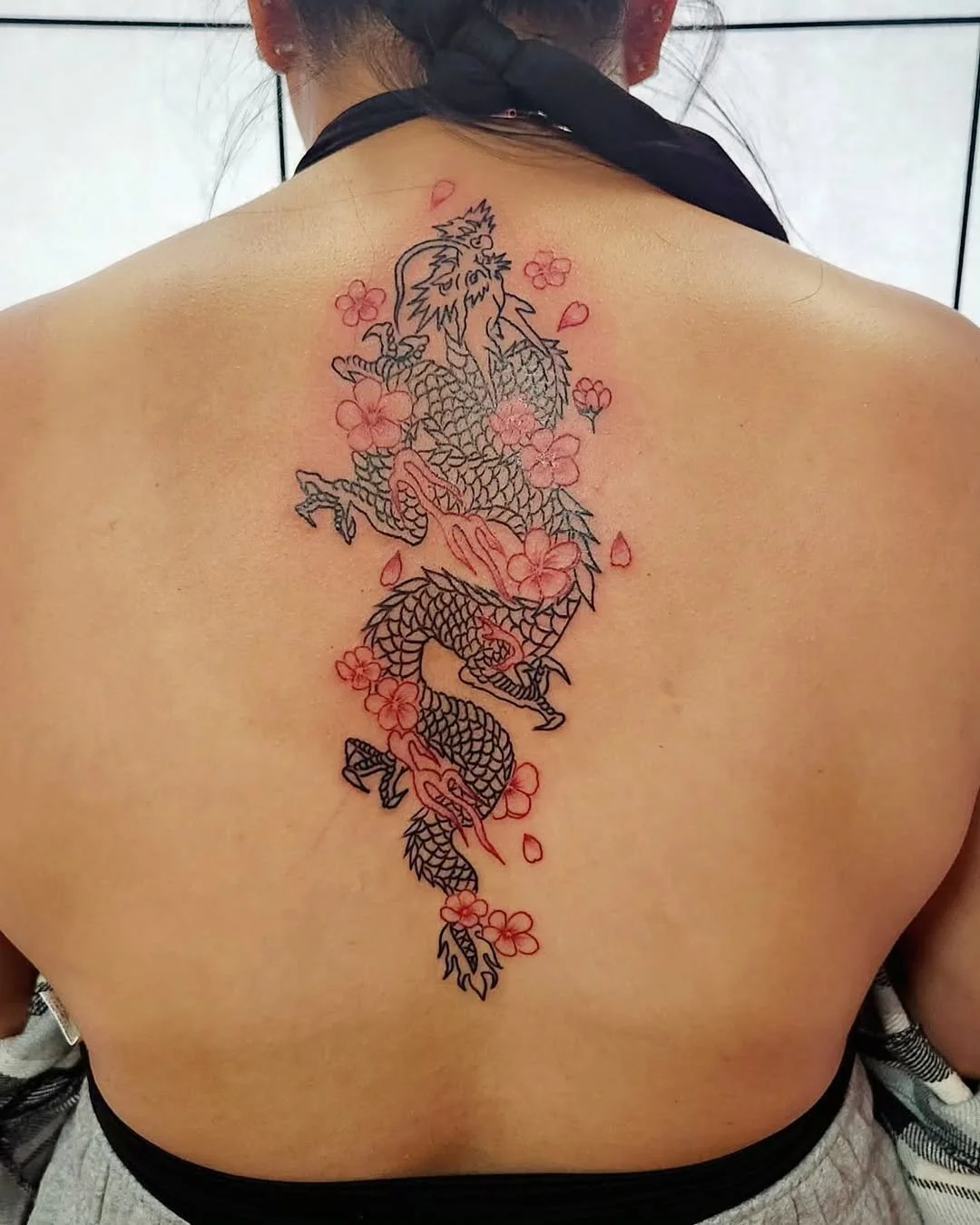 A tattoo of a dragon with cherry blossoms on a person's back.