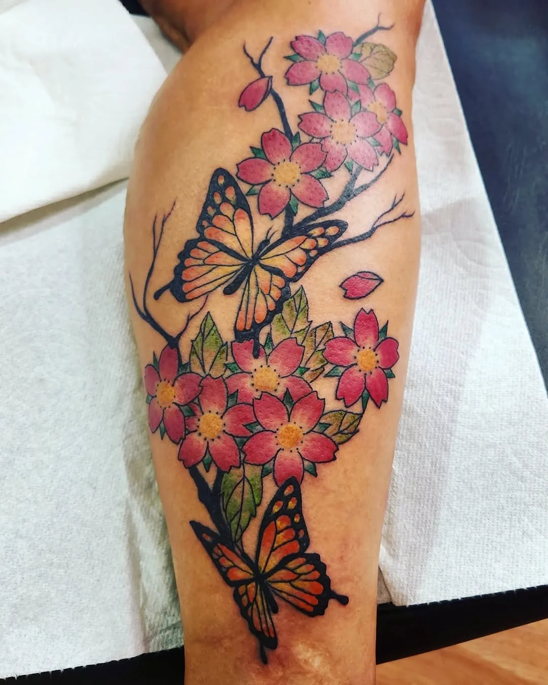 Colorful tattoo of pink cherry blossoms and orange monarch butterflies on a person's arm.