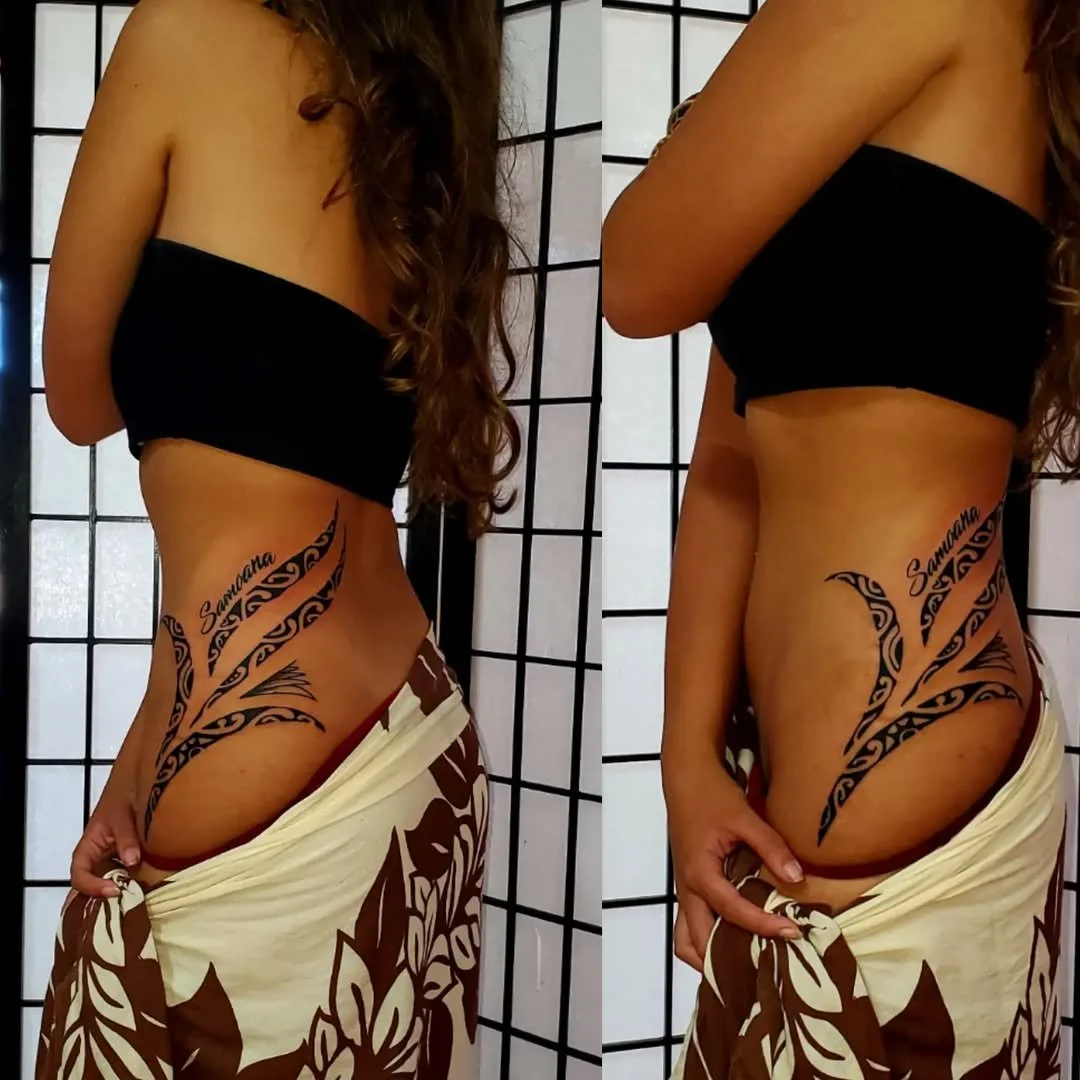 A woman with a side tattoo of tribal designs and the name 'Samantha' on her torso. She is wearing a black strapless top and a sarong with brown and white floral pattern, standing in front of a black grid screen.