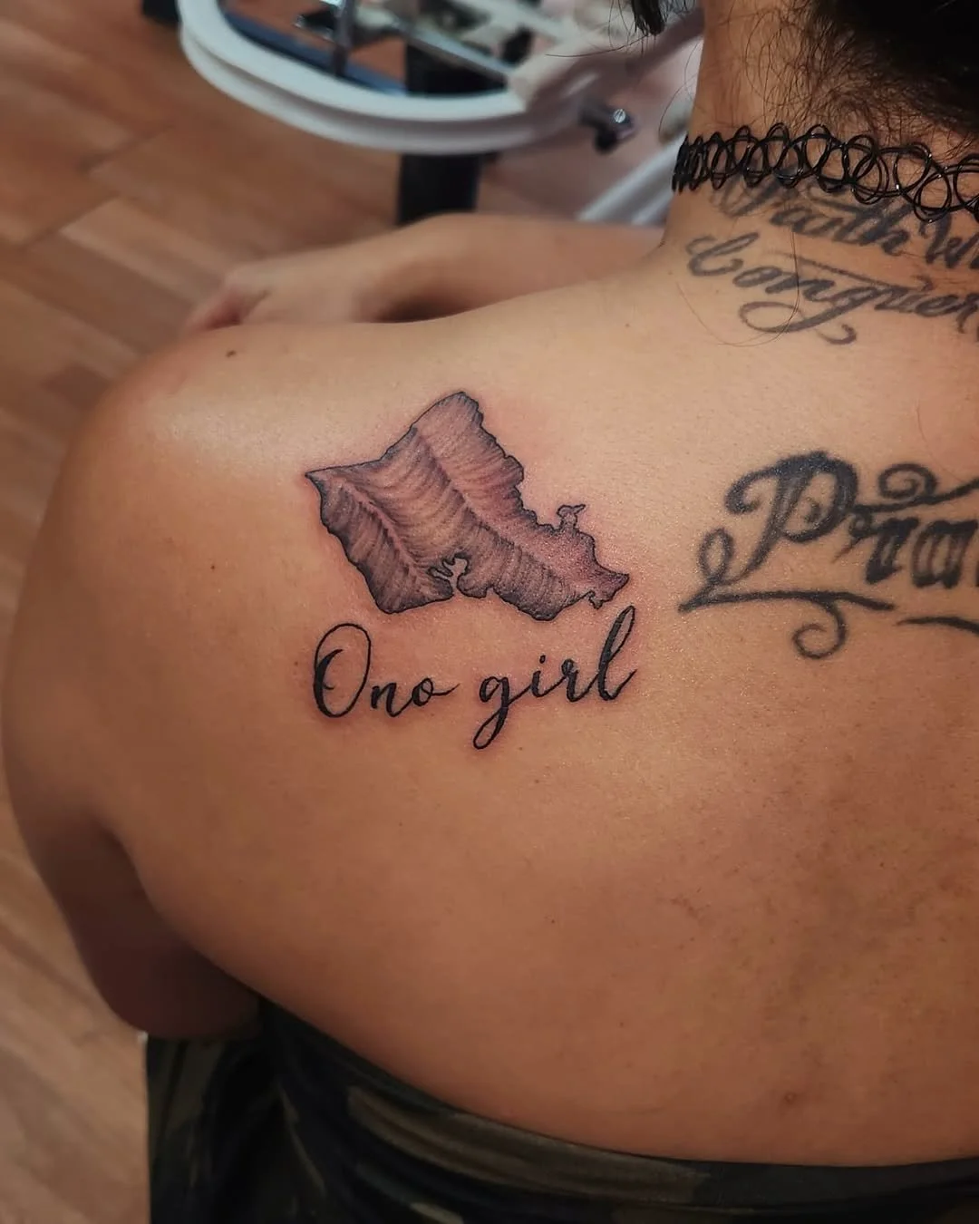 Tattoo of a coral-colored seashell with the words "Ono girl" written below it on a person's shoulder.