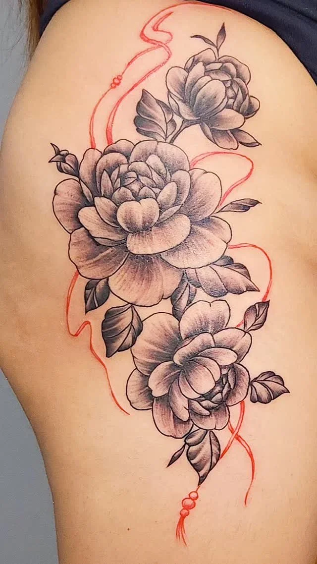 Black and gray floral tattoo with red decorative lines on person's upper arm/shoulder.