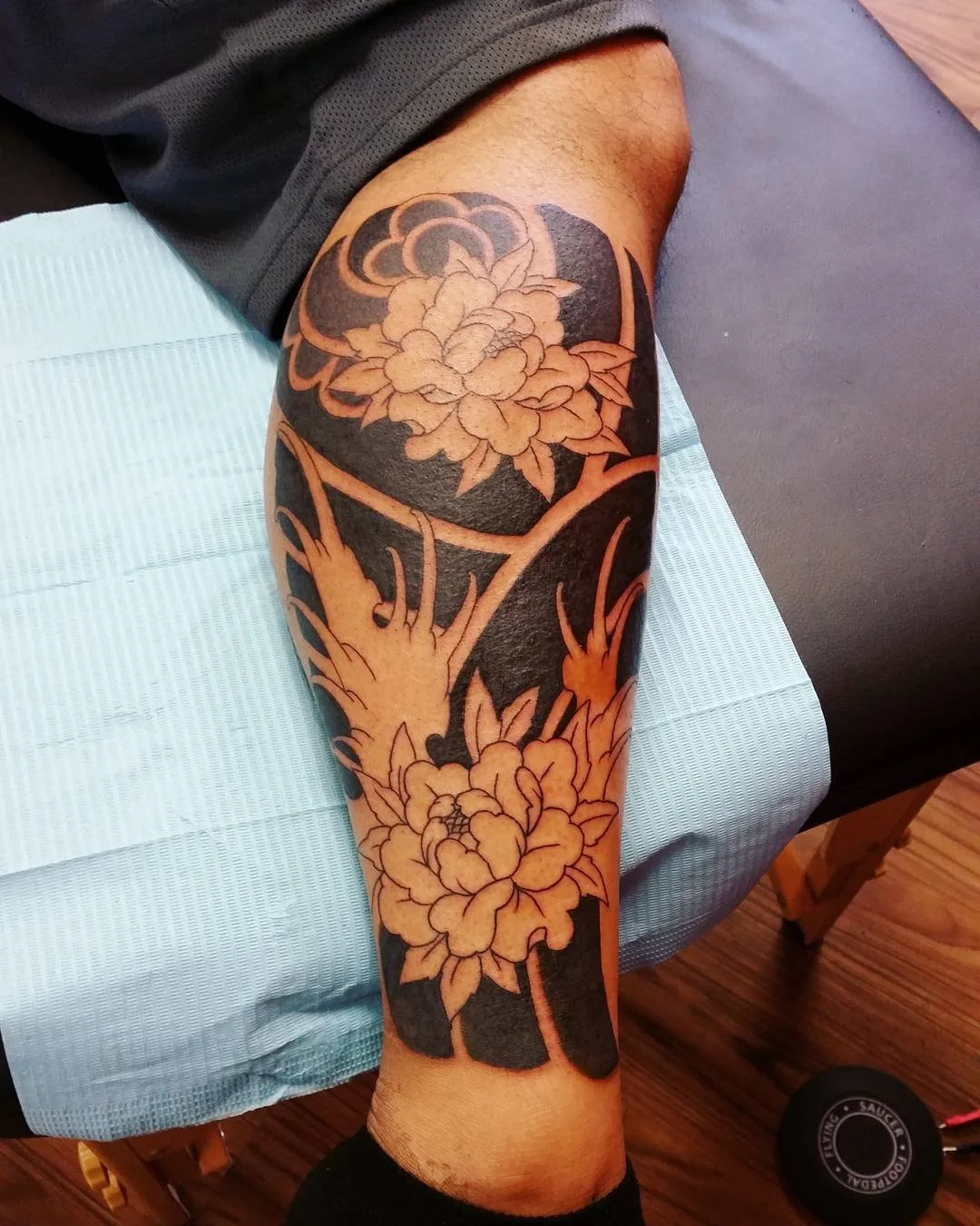Tattoo of a floral design with two large flowers and branches on a person’s arm.