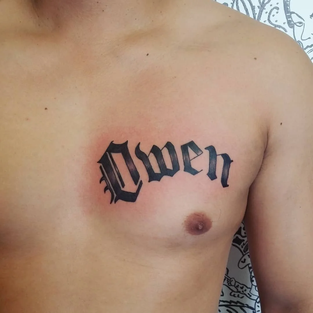 Tattoo of the word "Love" in black Gothic script on a person's chest.