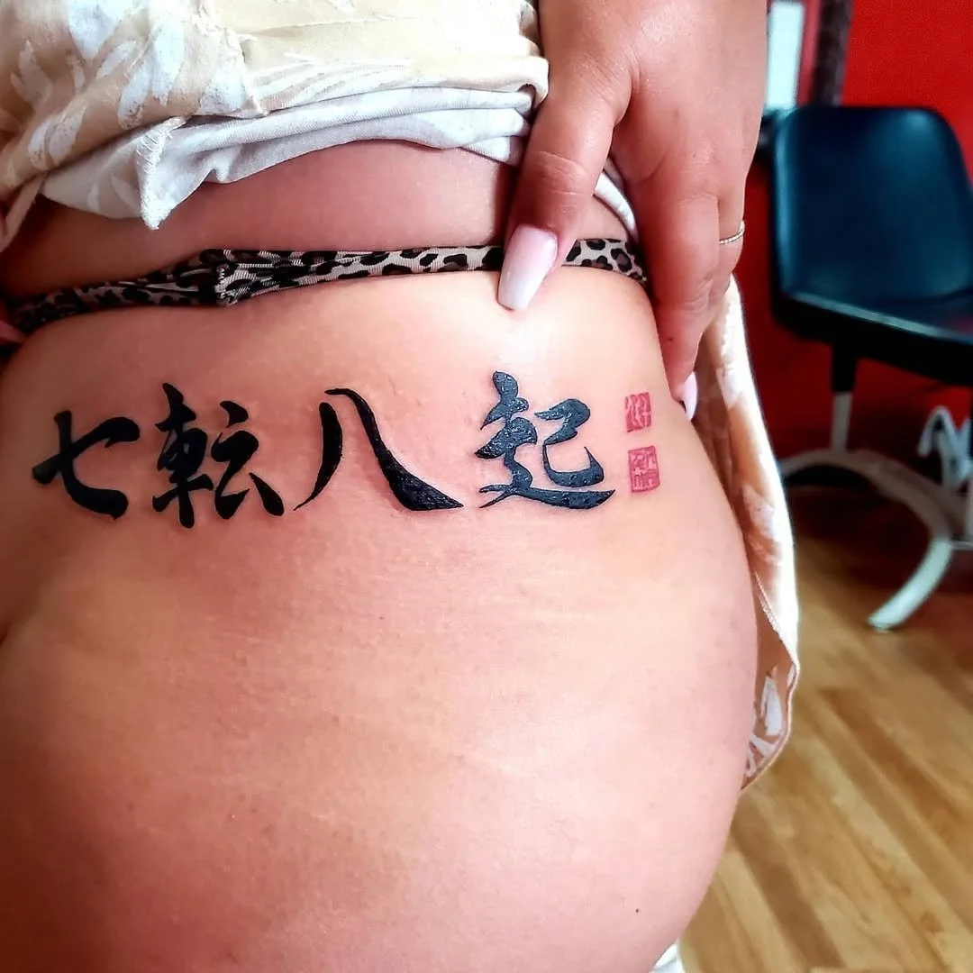 Tattoo in Chinese characters on a person's side, with two red stamps, partially visible leopard print clothing, and a hand pointing at the tattoo.