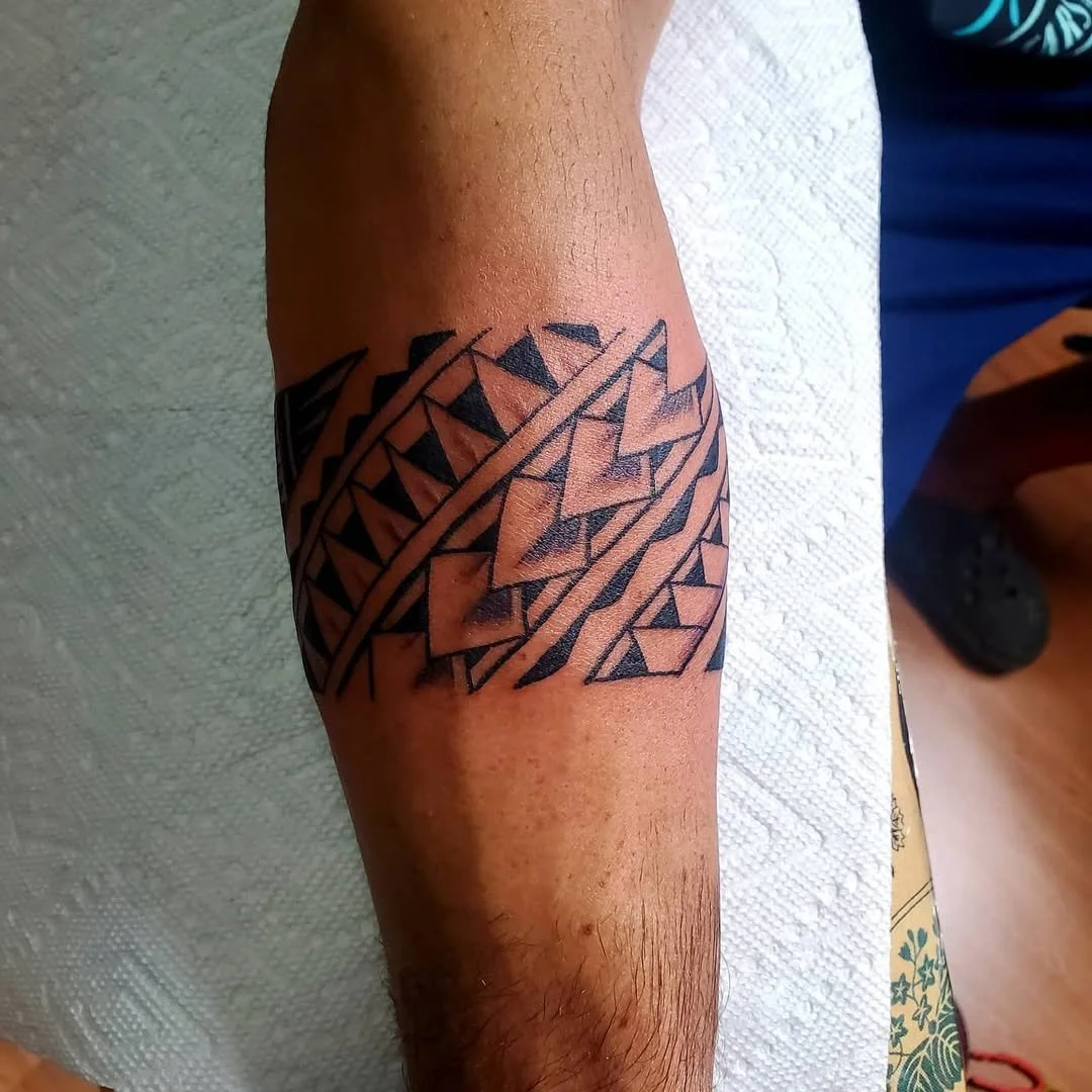 A black tribal style tattoo on a person's forearm featuring geometric shapes and lines.