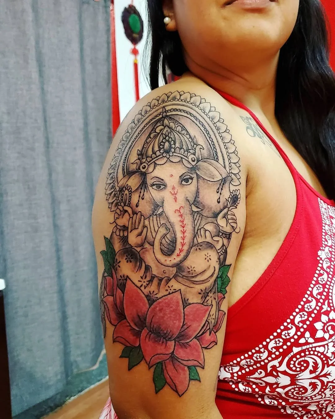 Tattoo of Lord Ganesha on woman's upper arm with a pink lotus flower at the bottom.
