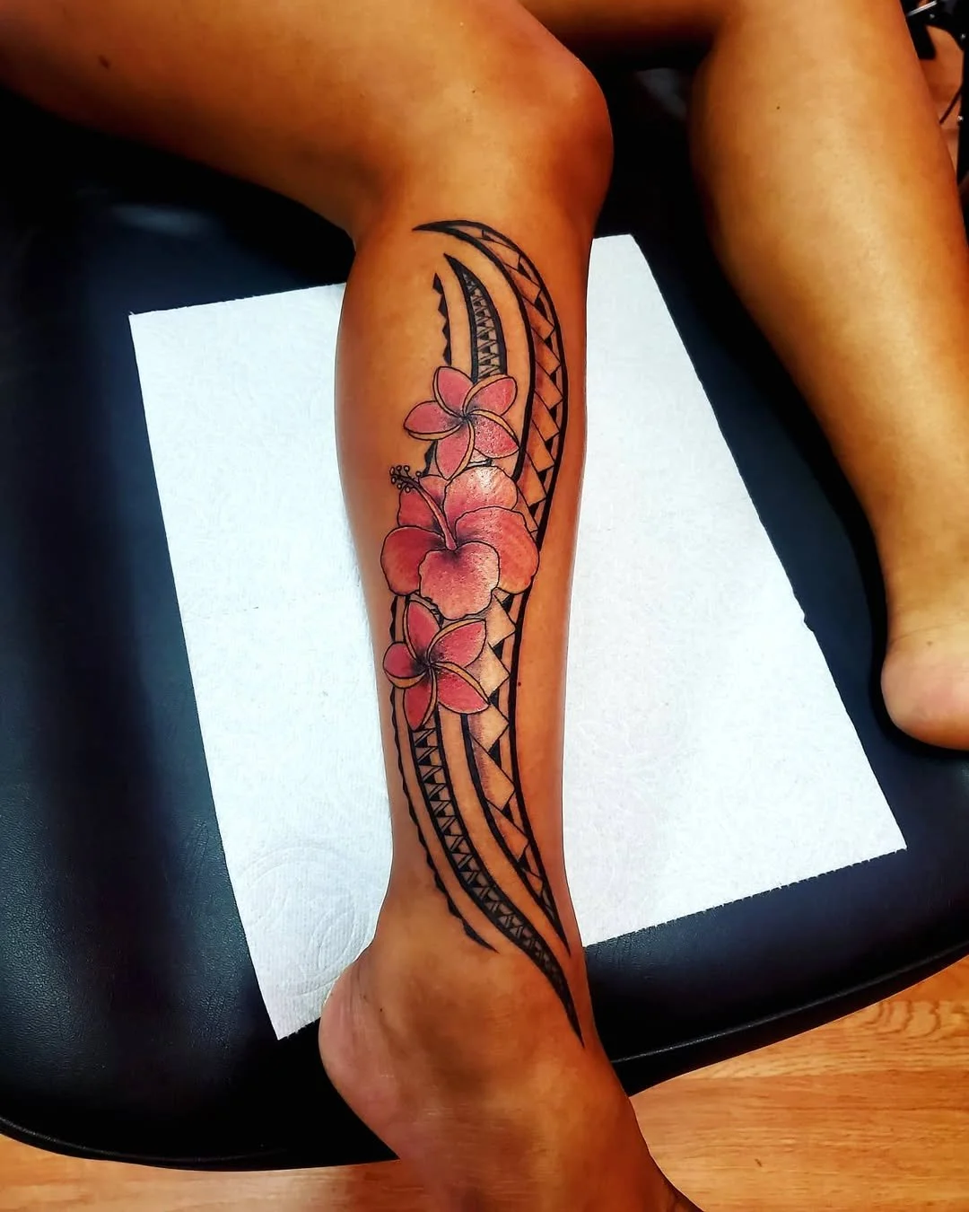 A person's leg with a tattoo of hibiscus flowers and tribal patterns.