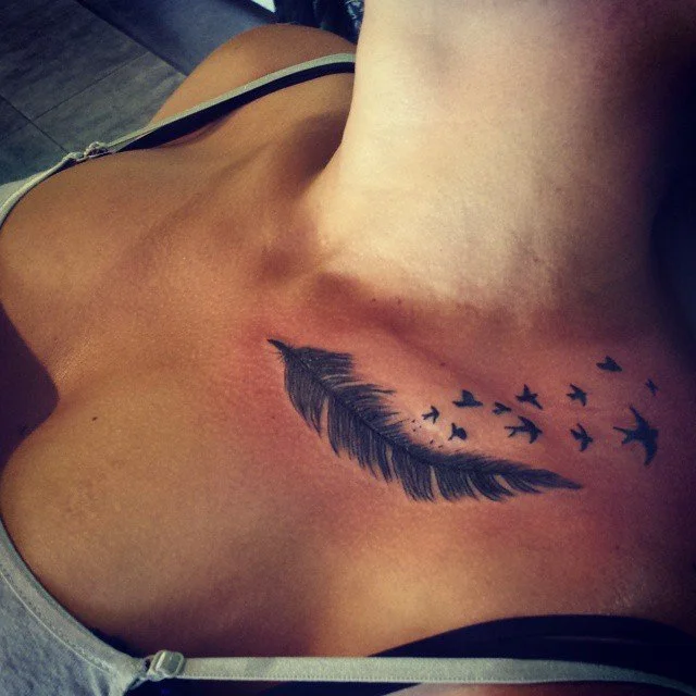 Tattoo of a black feather with birds flying away from it on a person's chest.