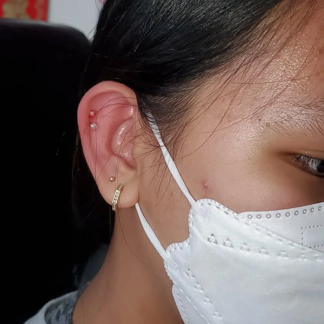 Close-up of a woman wearing a white face mask and multiple earrings on her ear.
