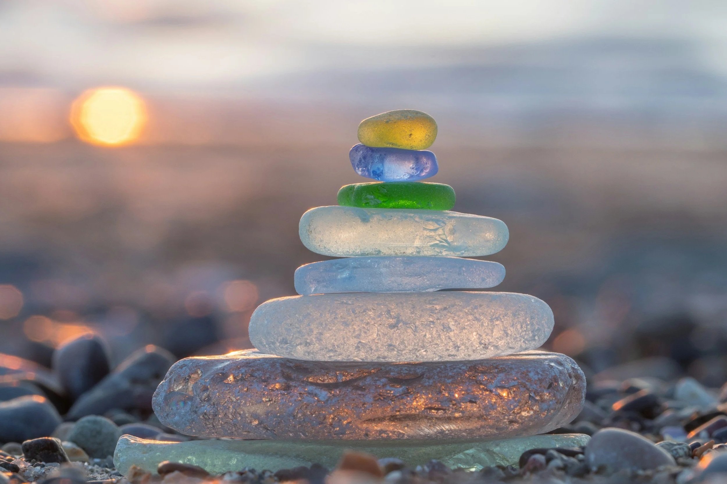 Stack of colorful sea glass stones on a pebble beach at sunset with the ocean in the background.