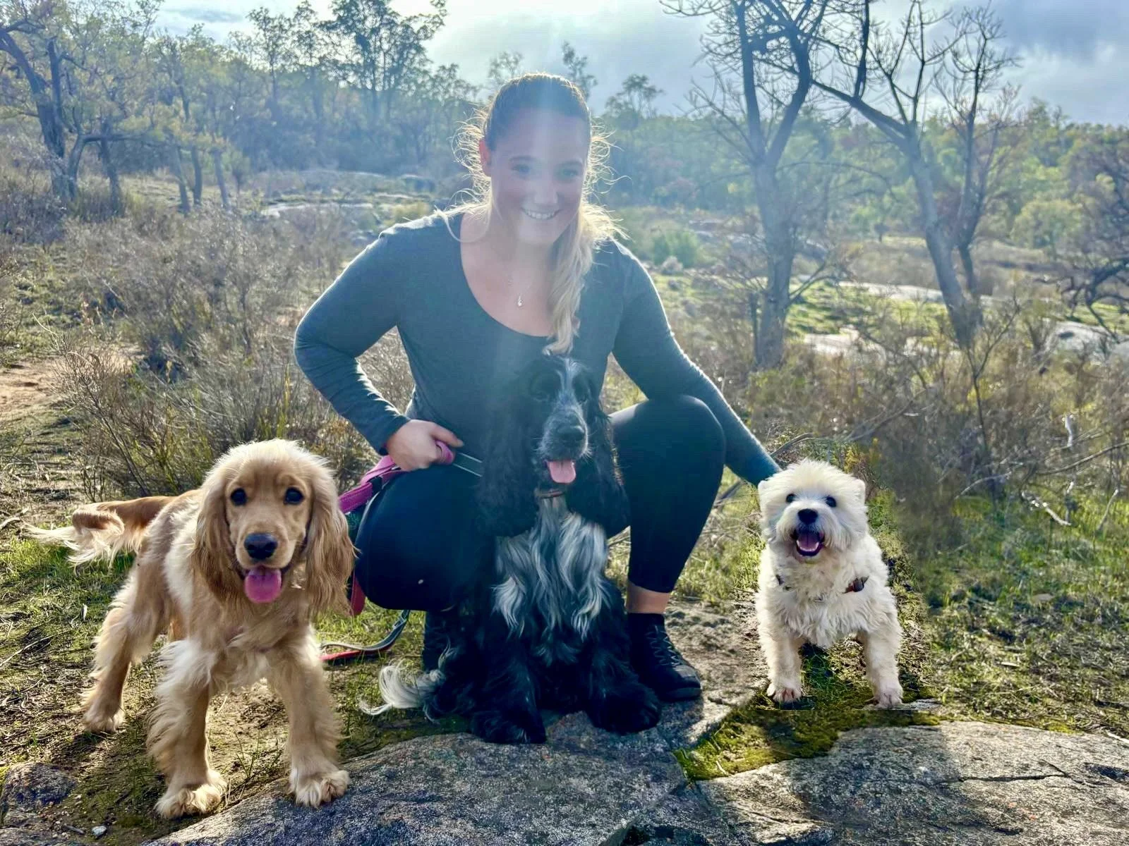 A woman with three dogs outdoors on a trail during daytime.