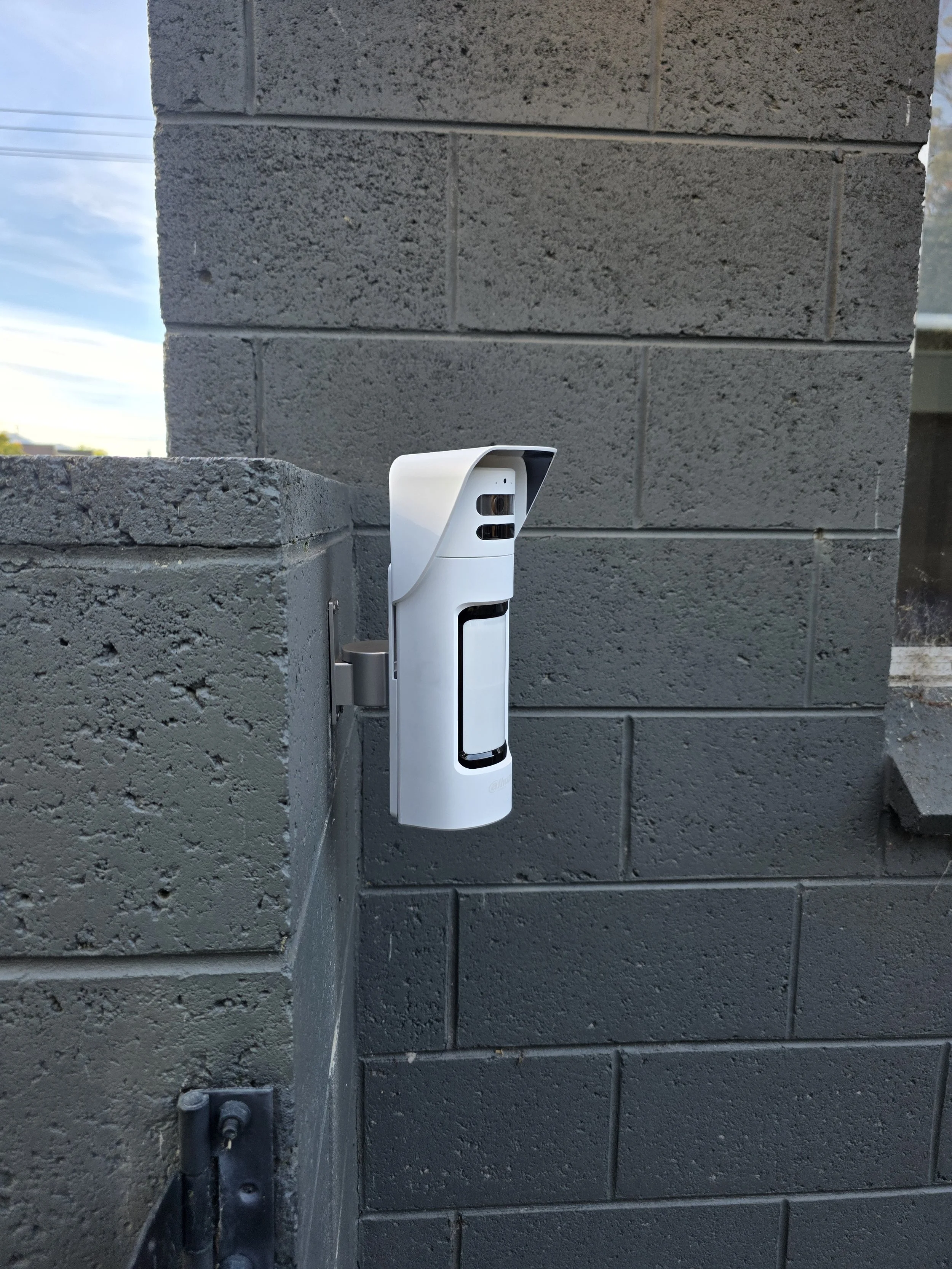 Security camera mounted on a gray brick wall outdoors.