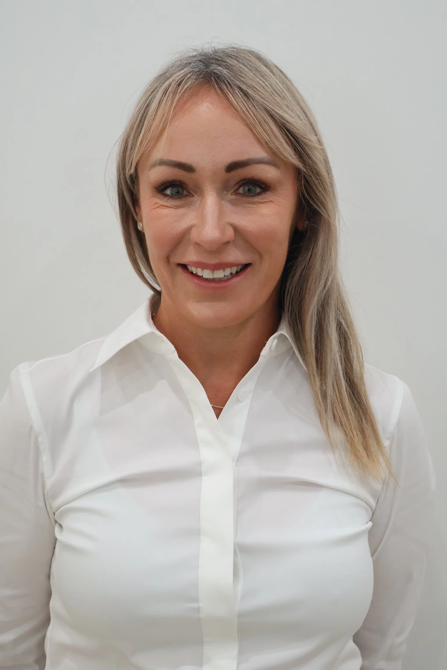A woman with blonde hair, wearing a white shirt, smiling at the camera against a plain white background. Skin Therapist Bowral, facial, laser, medifacial, cosmetic medicine, aesthetic medicine