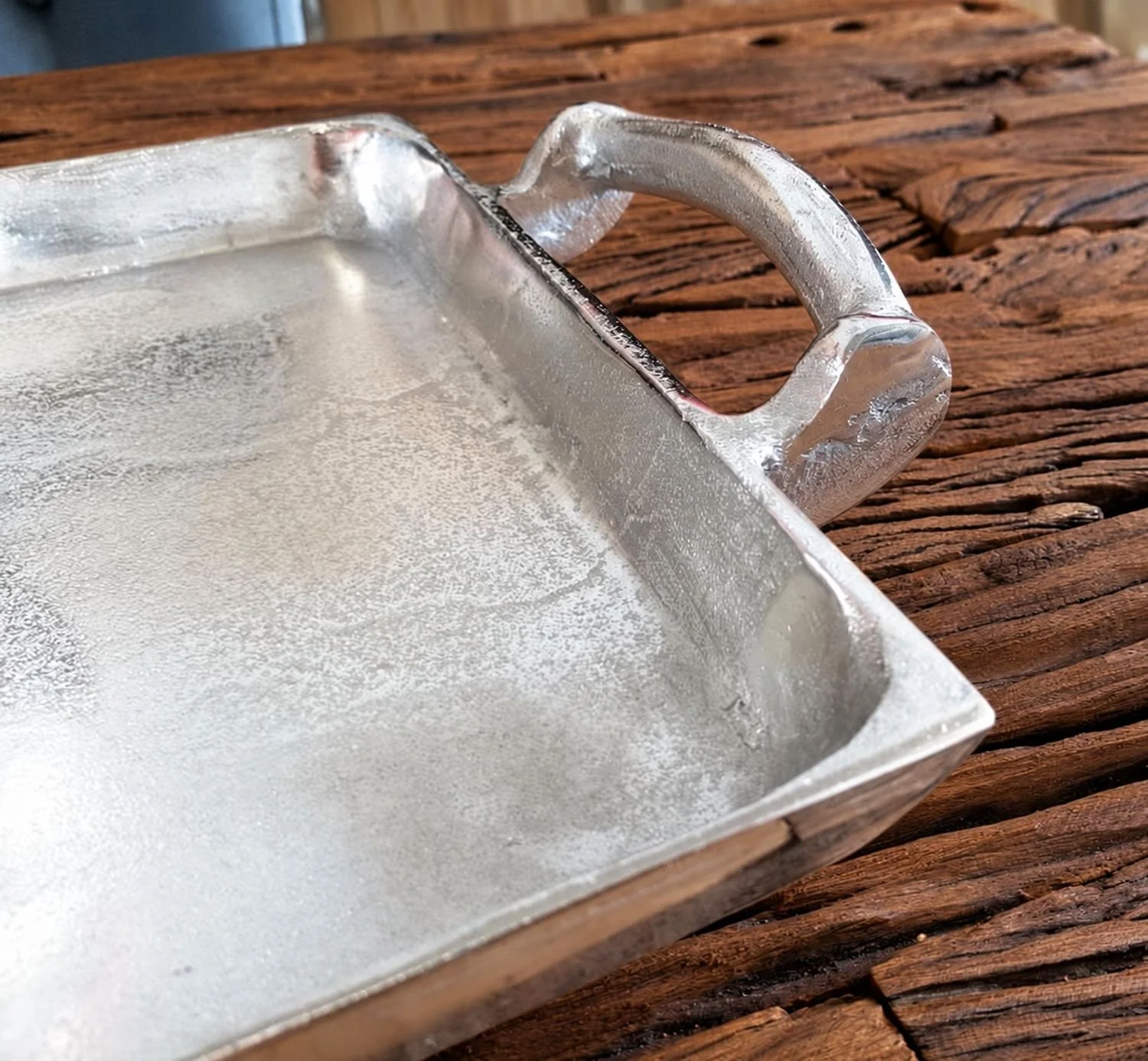 Närbild av aluminiumbrickans råa silverfärgade yta och handtag på ett mörkt träbord.