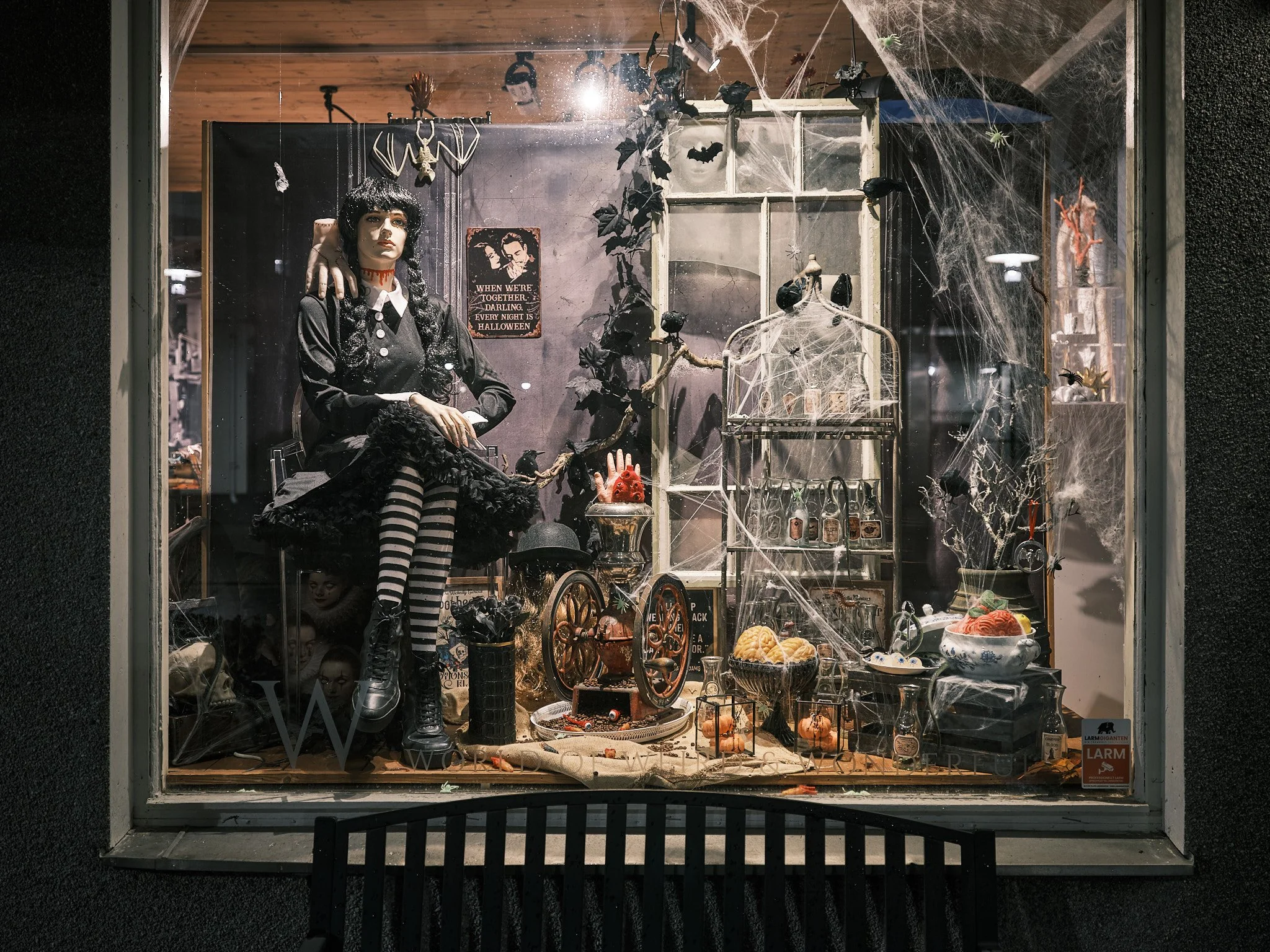 Halloween-utsmyckning med spindelväv, plastspindlar, pumpor, skrämmande leksaker, en docka med svart klänning och randiga strumpor, samt mörka dekorationer i fönstret.