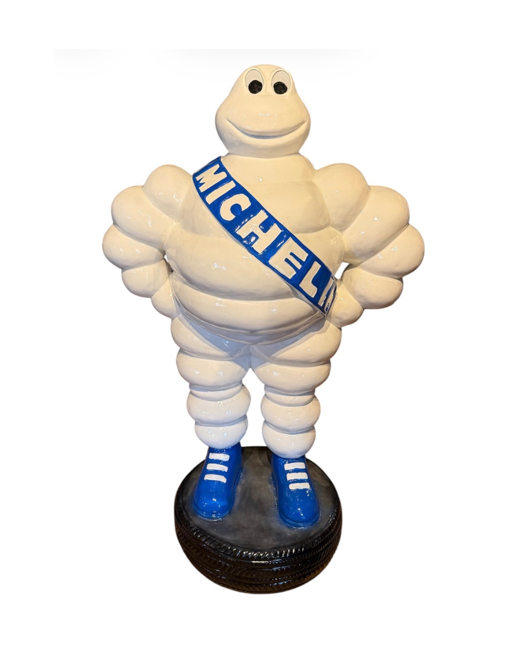 Vintage Michelingubben figur med blå Michelin-scarf stående på däcksockel.