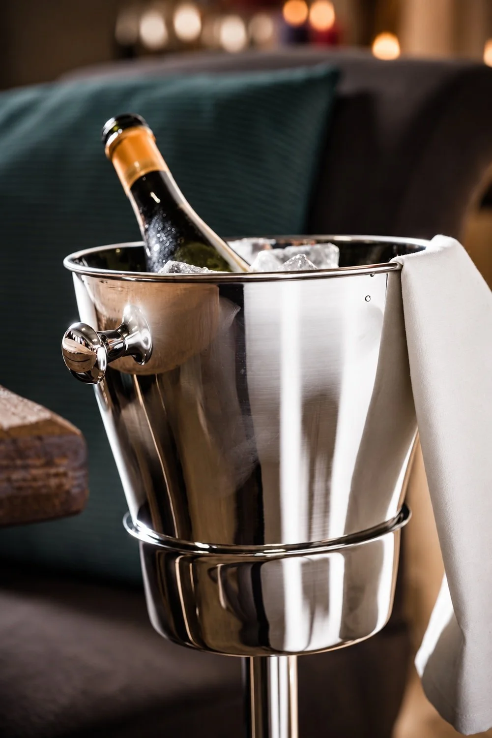 Närbild av champagnekylare i rostfritt stål med champagneflaska, is och vit servett över kanten.